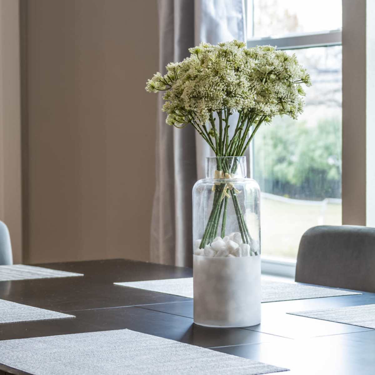 A dining table is set with light-colored placemats, and a glass vase filled with flowers sits at the center.