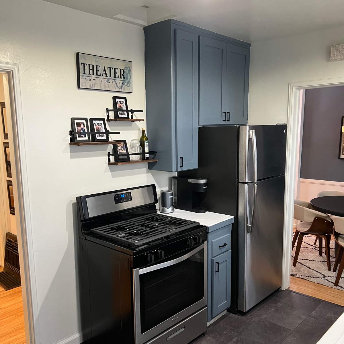 A modern kitchen features a gray stove and refrigerator, with navy blue cabinets and framed pictures on the wall.
