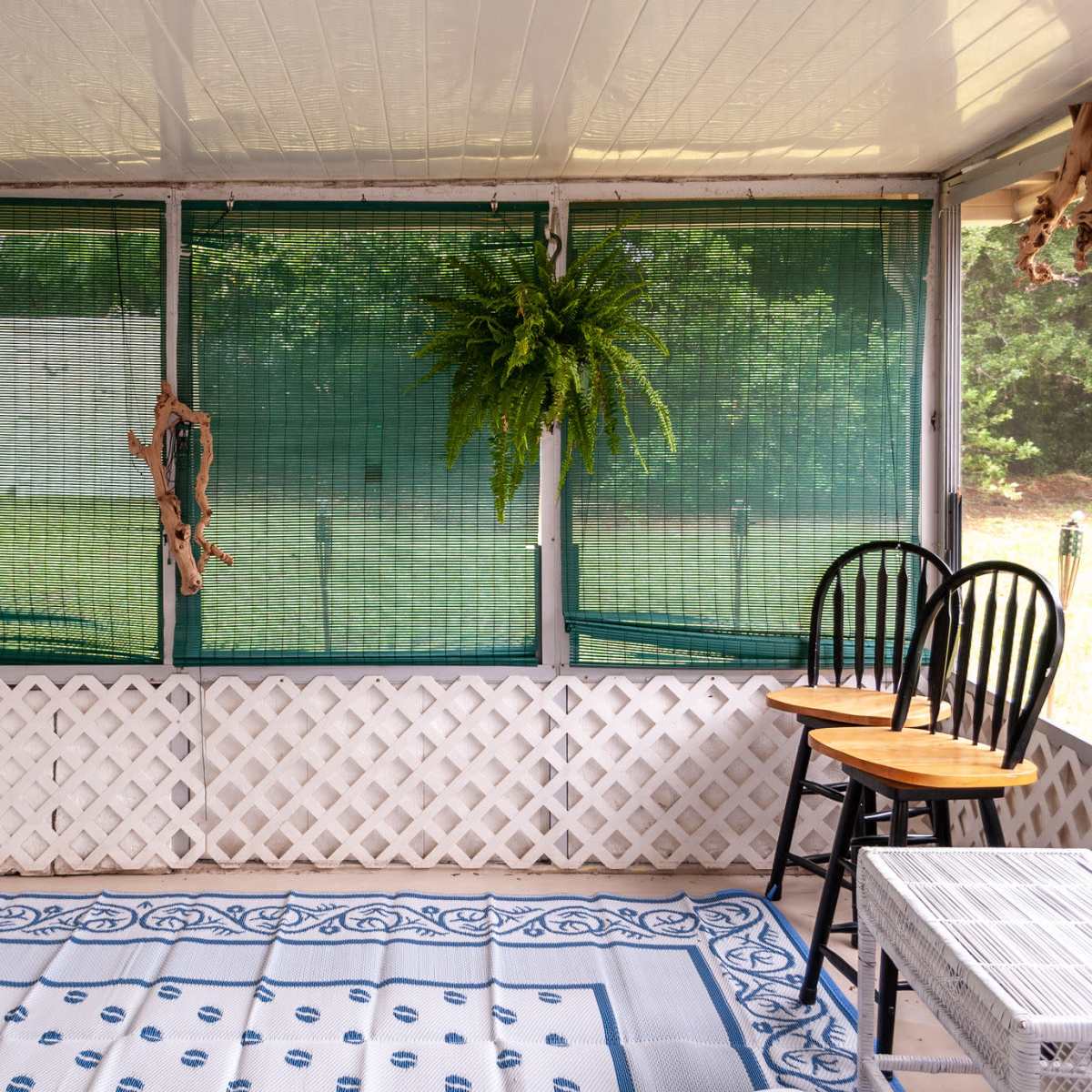 A screened porch with two hanging ferns, a decorative wall, and two wooden chairs.