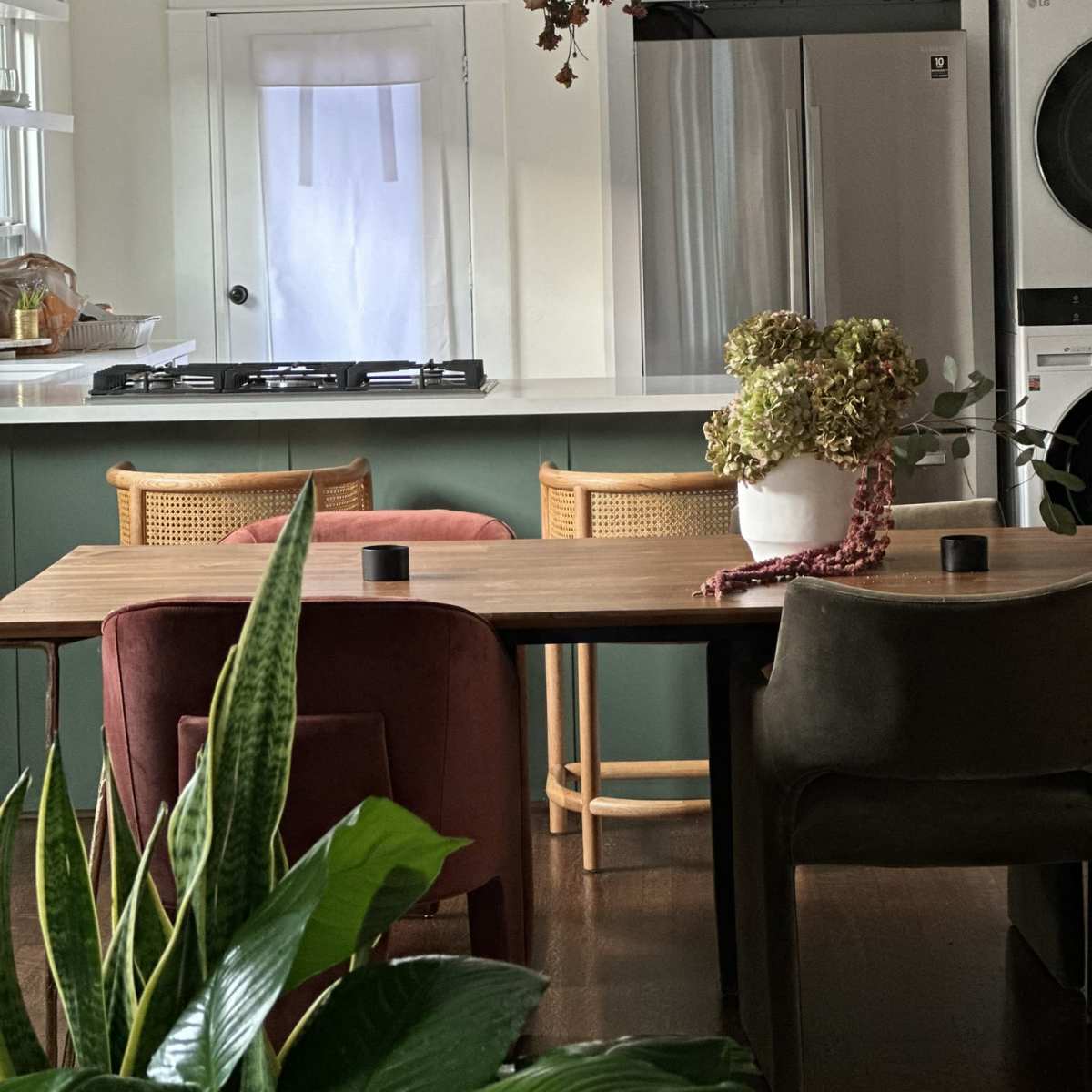 A kitchen and dining area with a wooden table surrounded by upholstered chairs, a large refrigerator, and a pendant light hanging above.