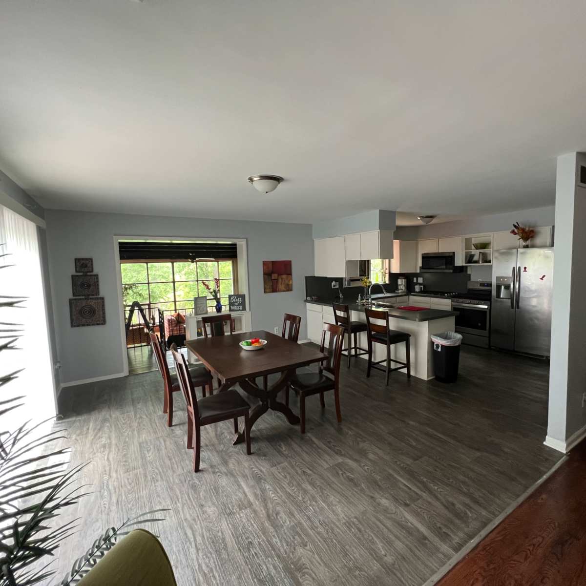 A spacious dining area with a wooden table and chairs next to a kitchen, featuring light gray walls and large windows.