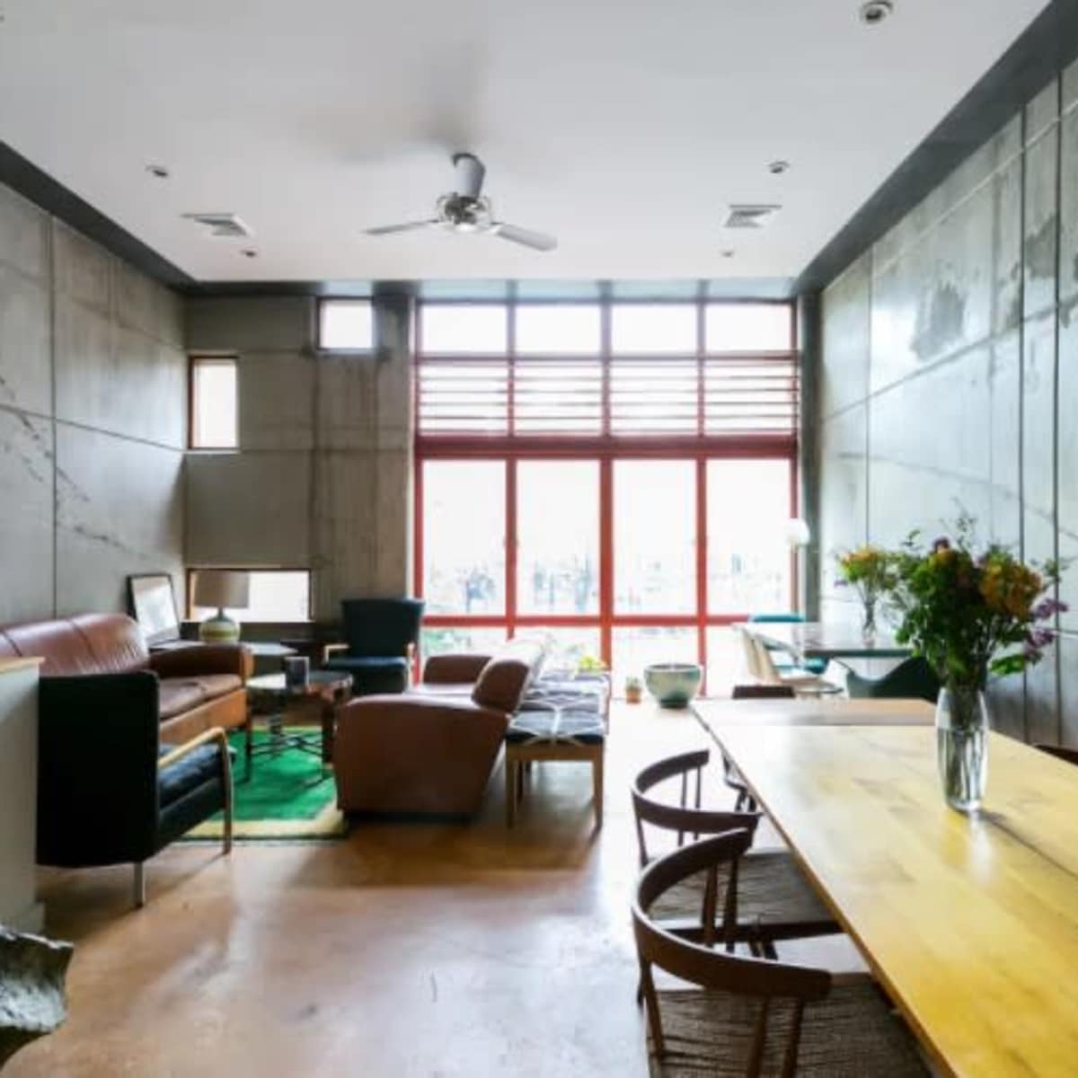A modern living space with concrete walls, a wooden dining table, and large windows allowing natural light to enter.