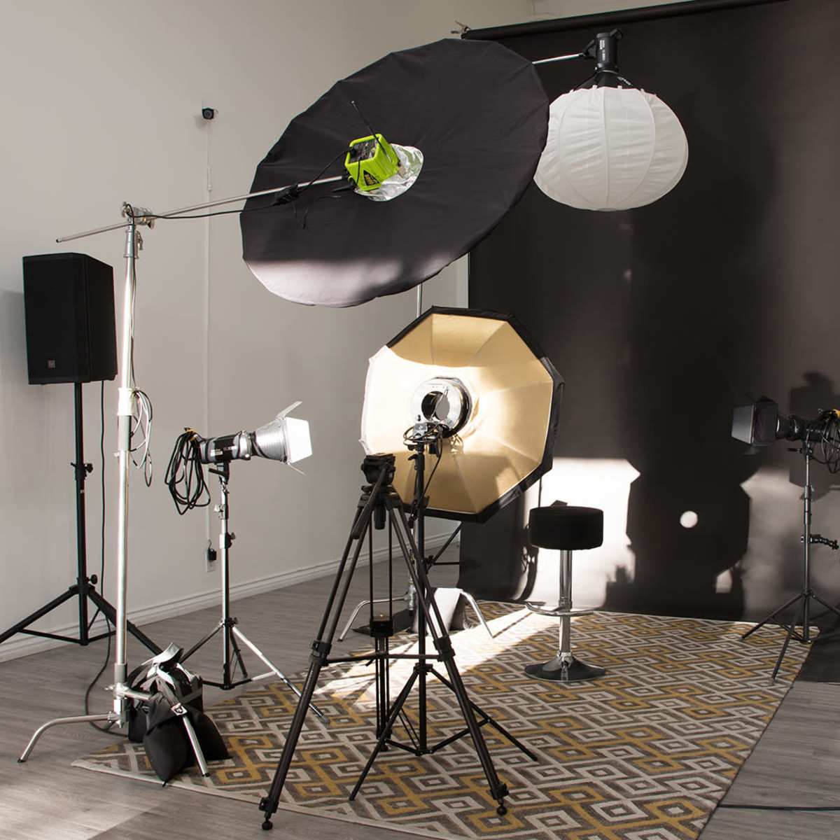 A photography studio set up with various lighting equipment, backdrops, and a stool on a patterned rug.