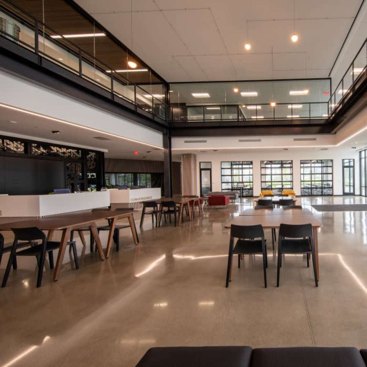 A modern, open lobby area with polished concrete floors, multiple seating arrangements, and large glass windows allowing natural light to flood the space.