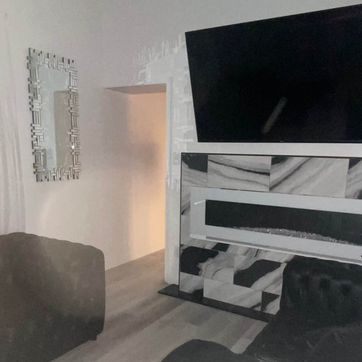 A dimly lit living room with black leather sofas, a large television mounted on the wall, and a decorative mirror.