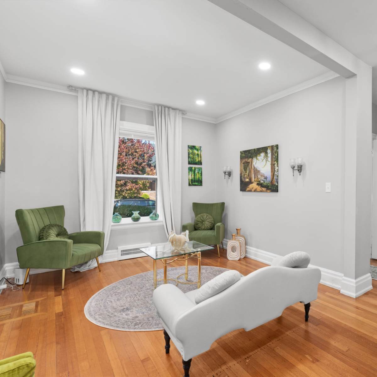 A well-lit living room with two green armchairs, a coffee table, and hardwood flooring, featuring a frosted glass door leading to another room.