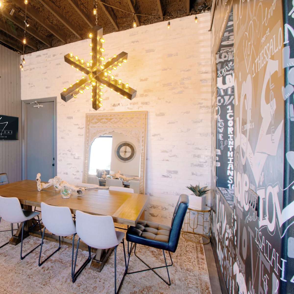 A dining area features a wooden table with white and black chairs, illuminated by a star-shaped light fixture against a textured wall.