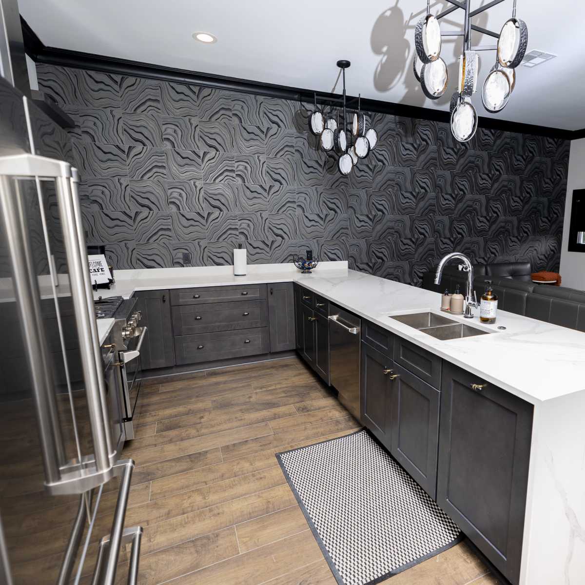 A modern kitchen with a central island, dark cabinetry, and a patterned accent wall.