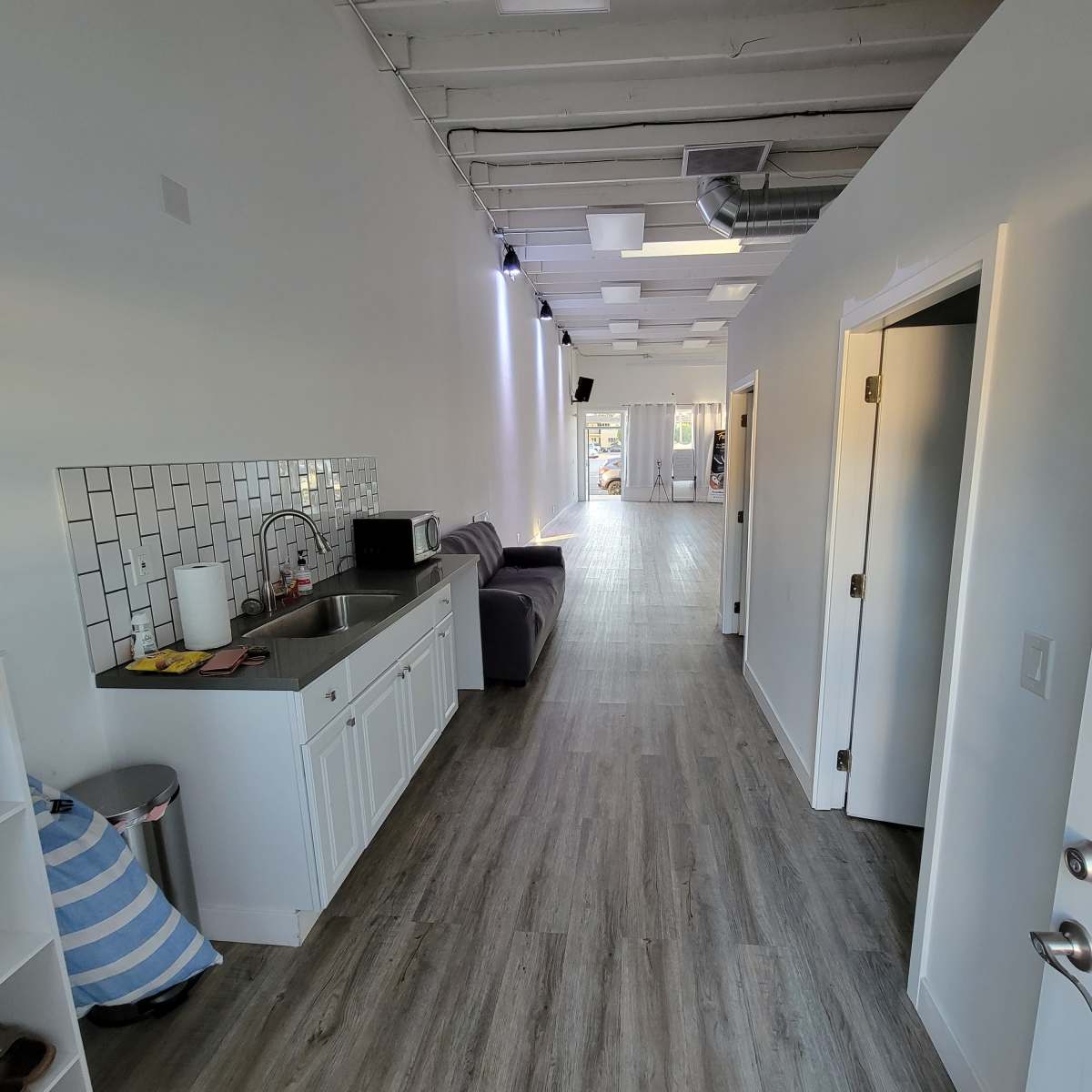 A modern corridor with a kitchen area on the left, hardwood flooring, and doors leading to different rooms.