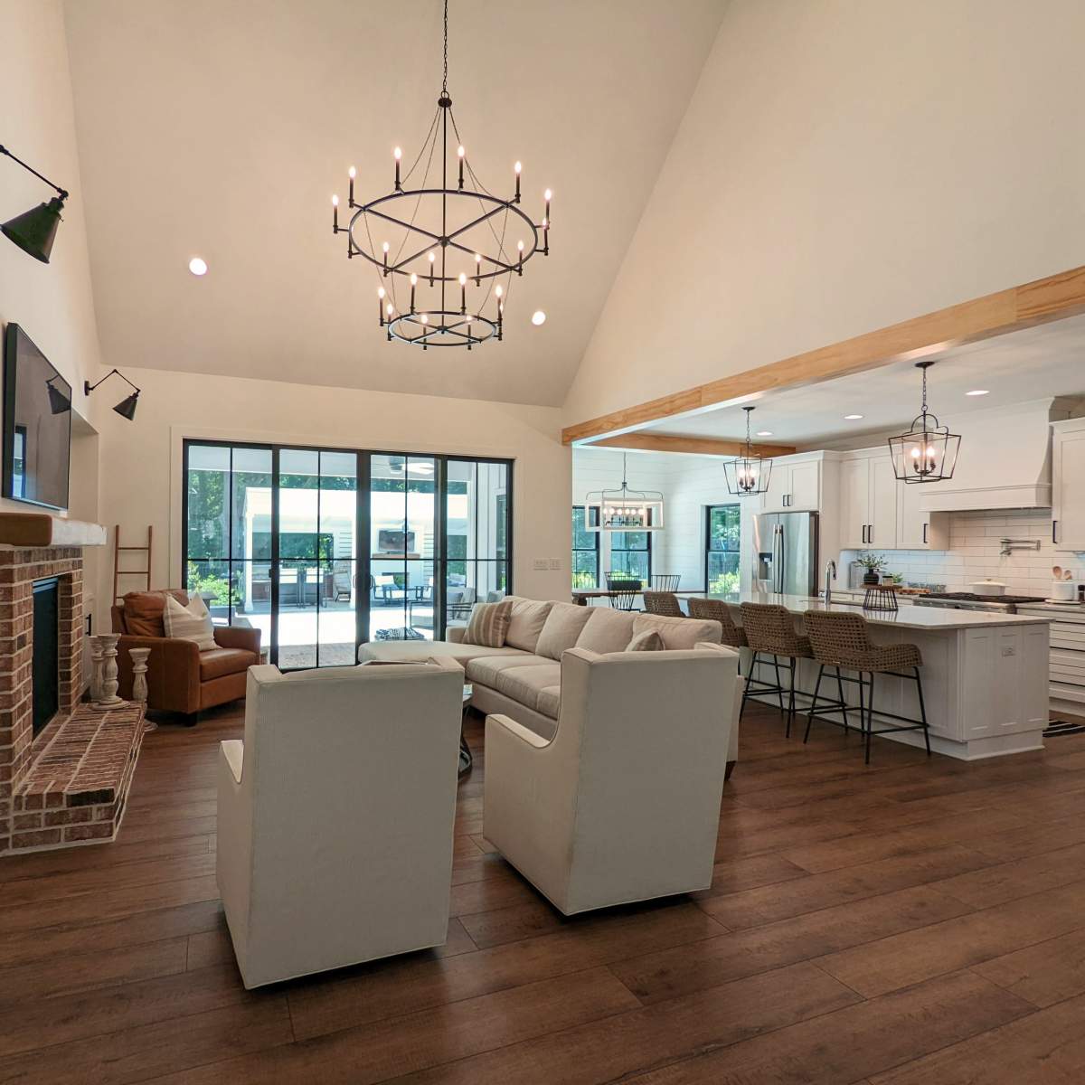 A spacious living area with a high ceiling, featuring a combination of a seating arrangement, a fireplace, and an open kitchen with bar seating.