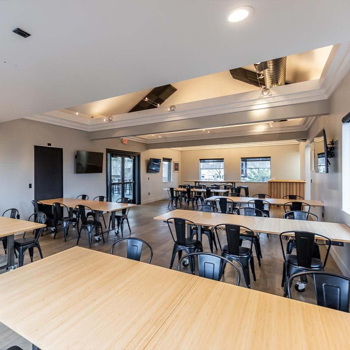 A spacious meeting room features multiple tables arranged for group seating, with large windows allowing natural light.