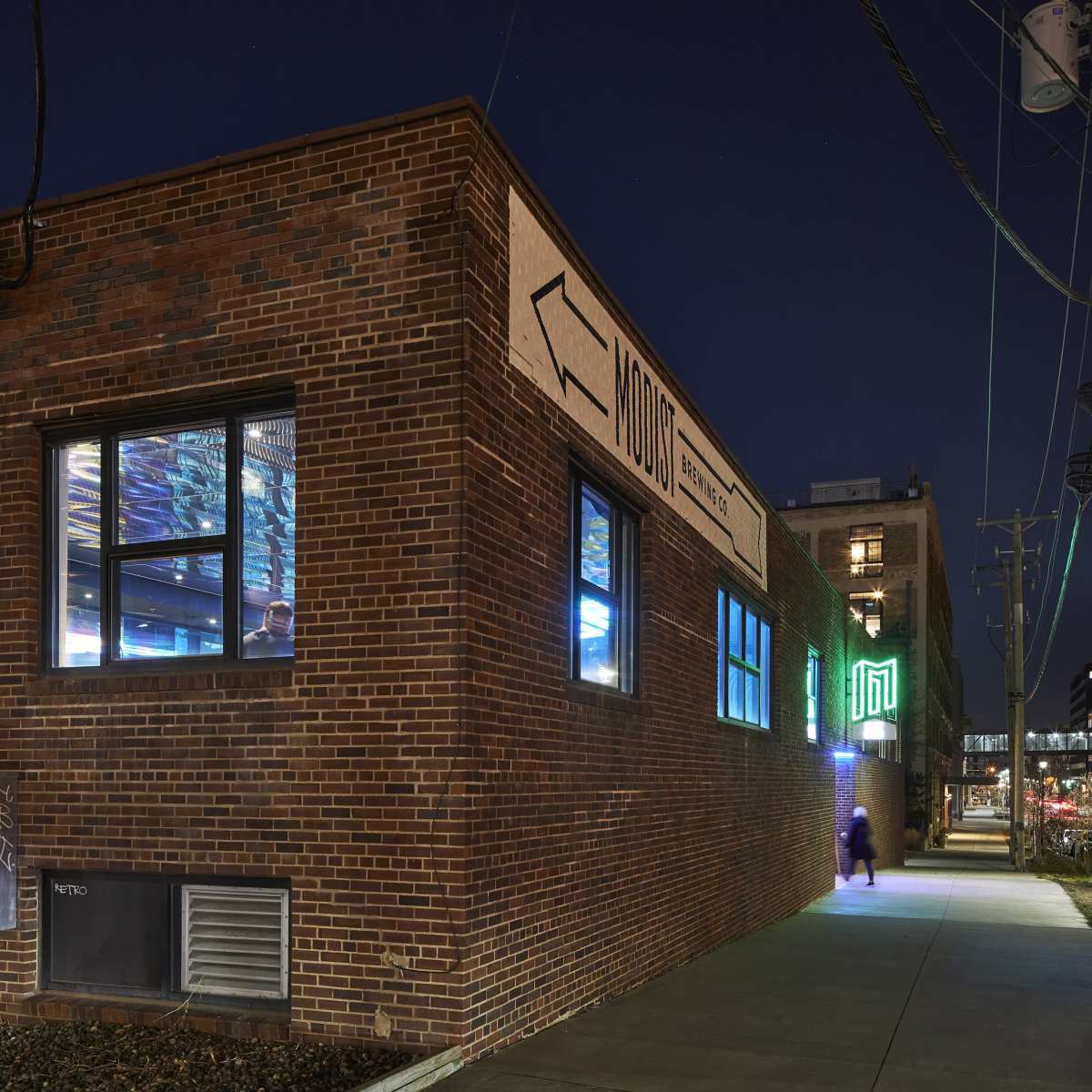 A brick building at night features illuminated signs and a sidewalk leading away from it.