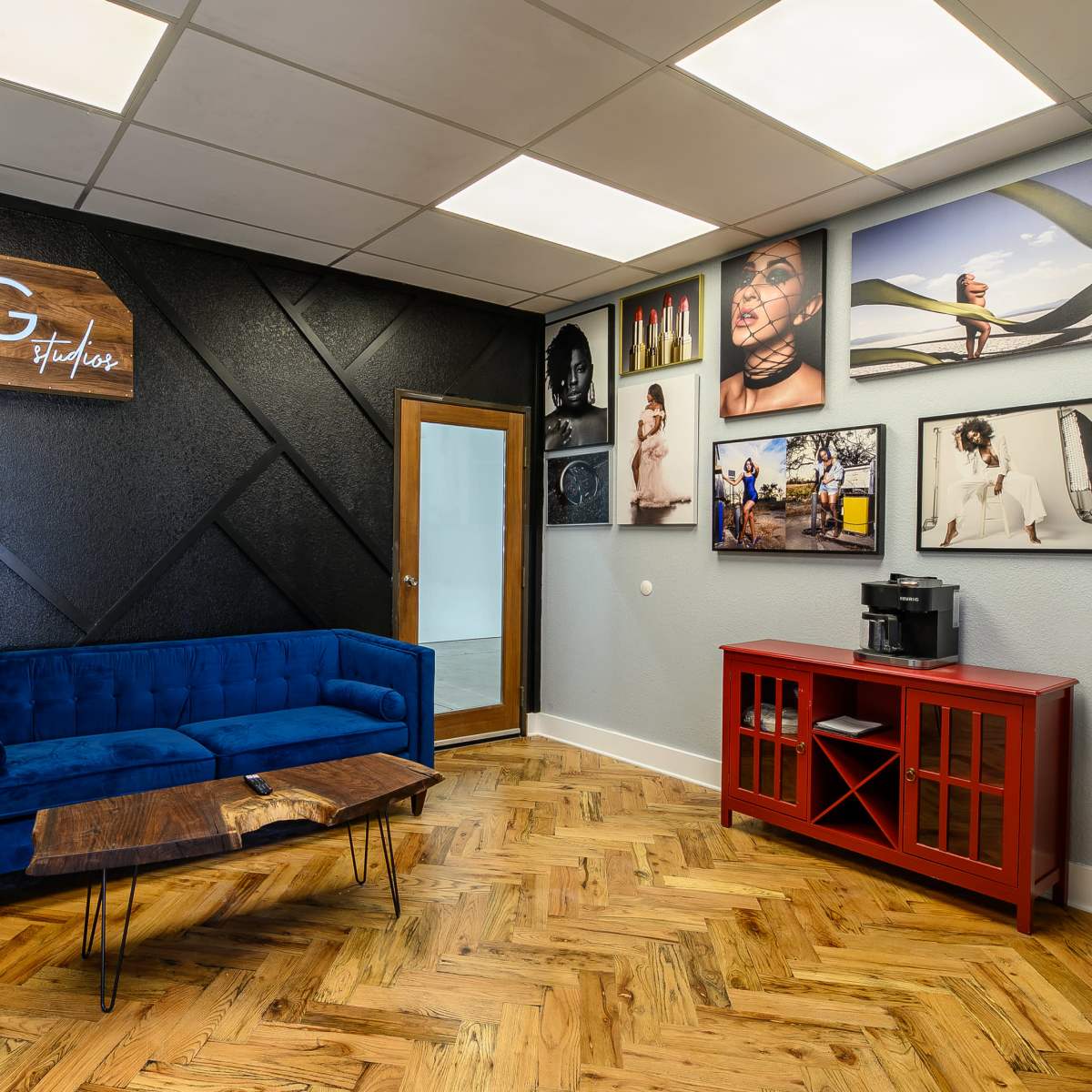 A modern studio interior with a blue sofa, a wooden coffee table, and various framed photographs on the walls.