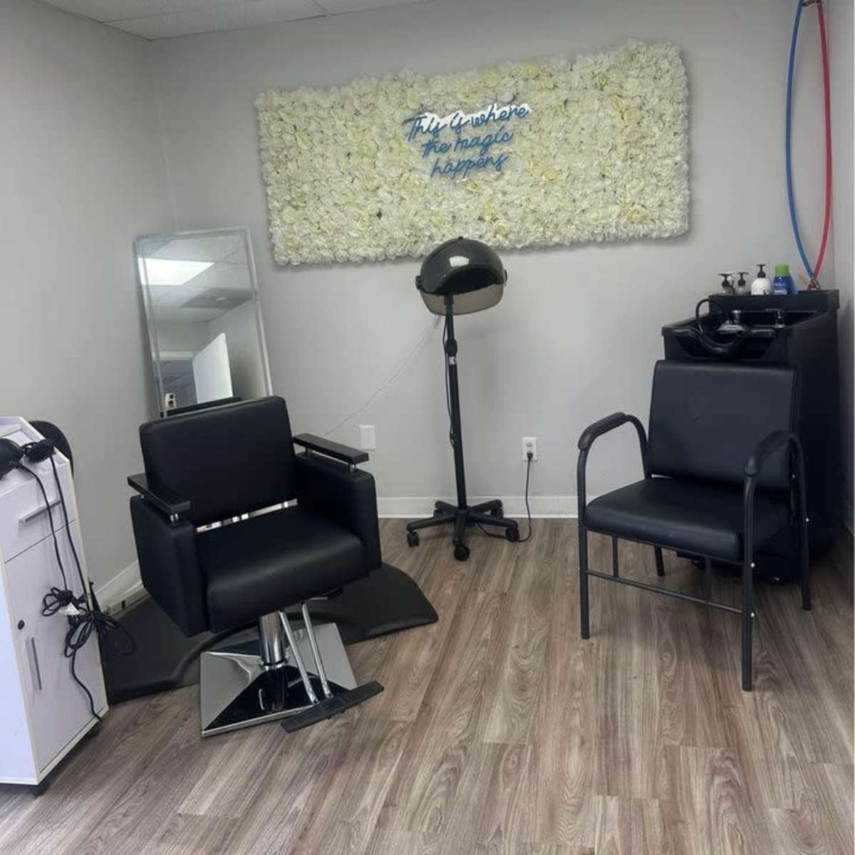 A hair salon interior with two black salon chairs, a mirror, and a wall decorated with artificial flowers.