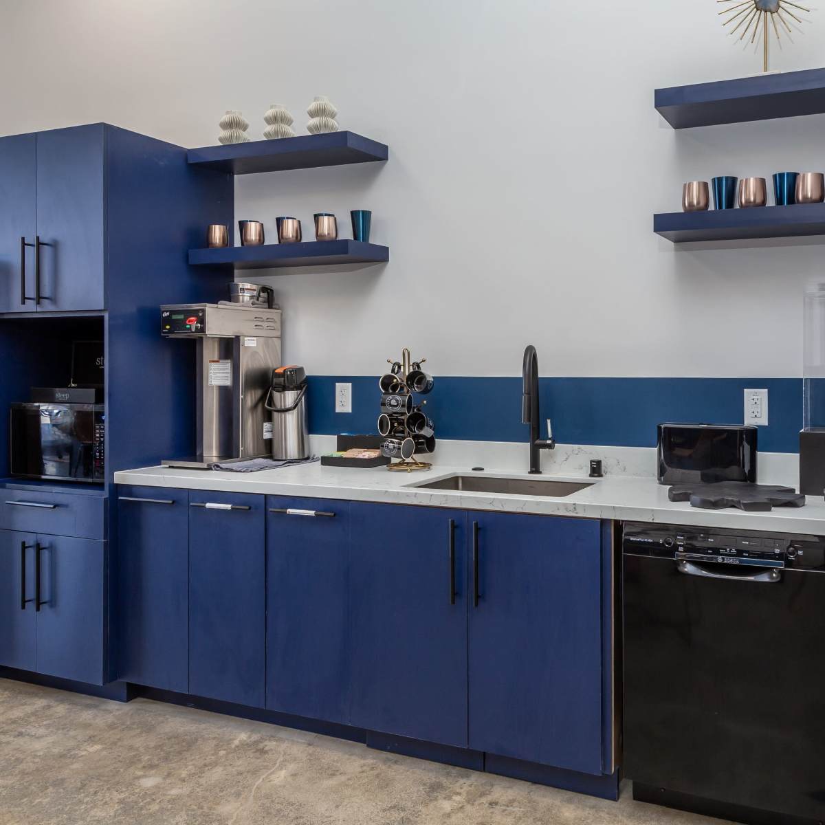 A modern kitchen area featuring blue cabinetry, a stainless steel sink, a coffee machine, and a microwave on the counter.