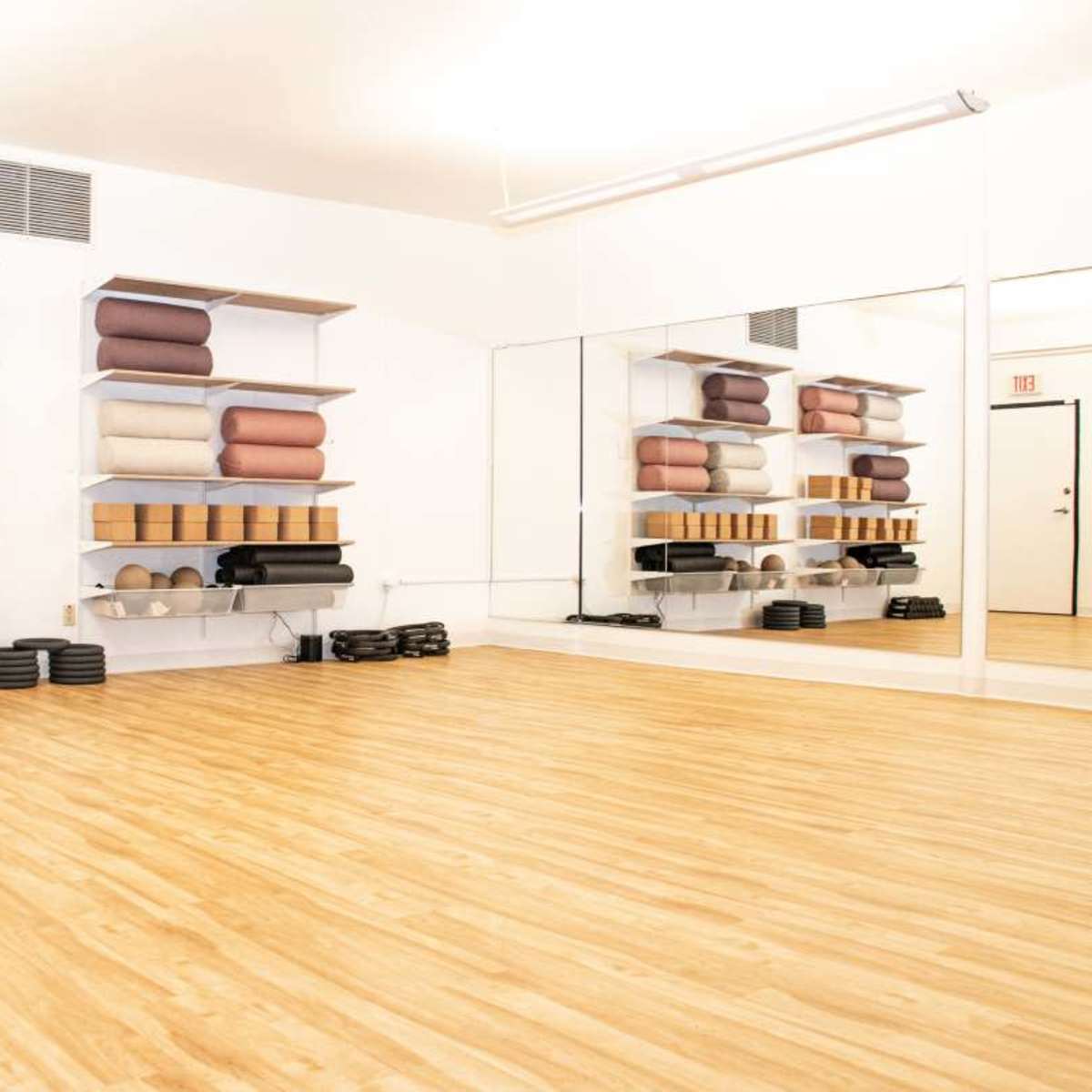 A spacious, empty yoga studio with neatly arranged shelves holding various yoga accessories against white walls.