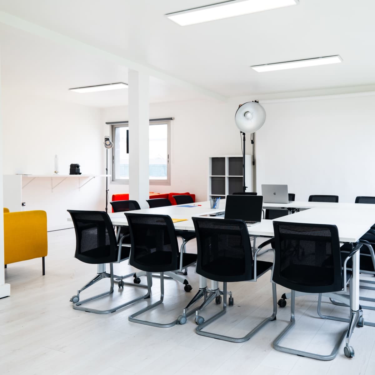 A modern conference room features a long table surrounded by black rolling chairs, with large windows and minimalistic decor.