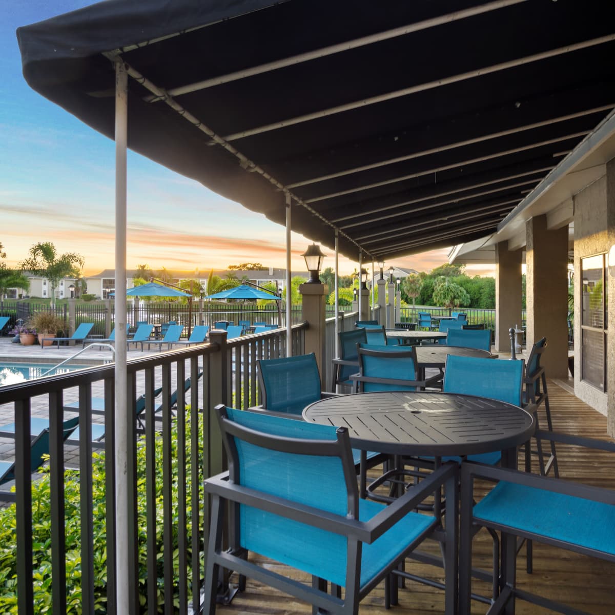 A patio area with turquoise chairs and tables overlooking a swimming pool at sunset.