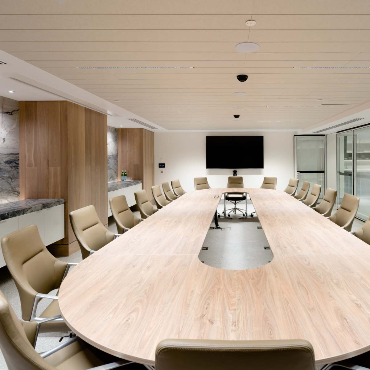 A modern conference room featuring a large oval table surrounded by leather chairs and a wall-mounted screen.