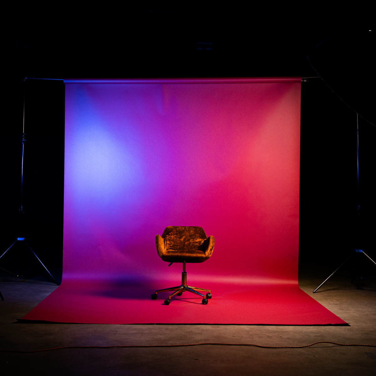A rolling office chair is centered in front of a gradient backdrop that transitions from blue to pink.