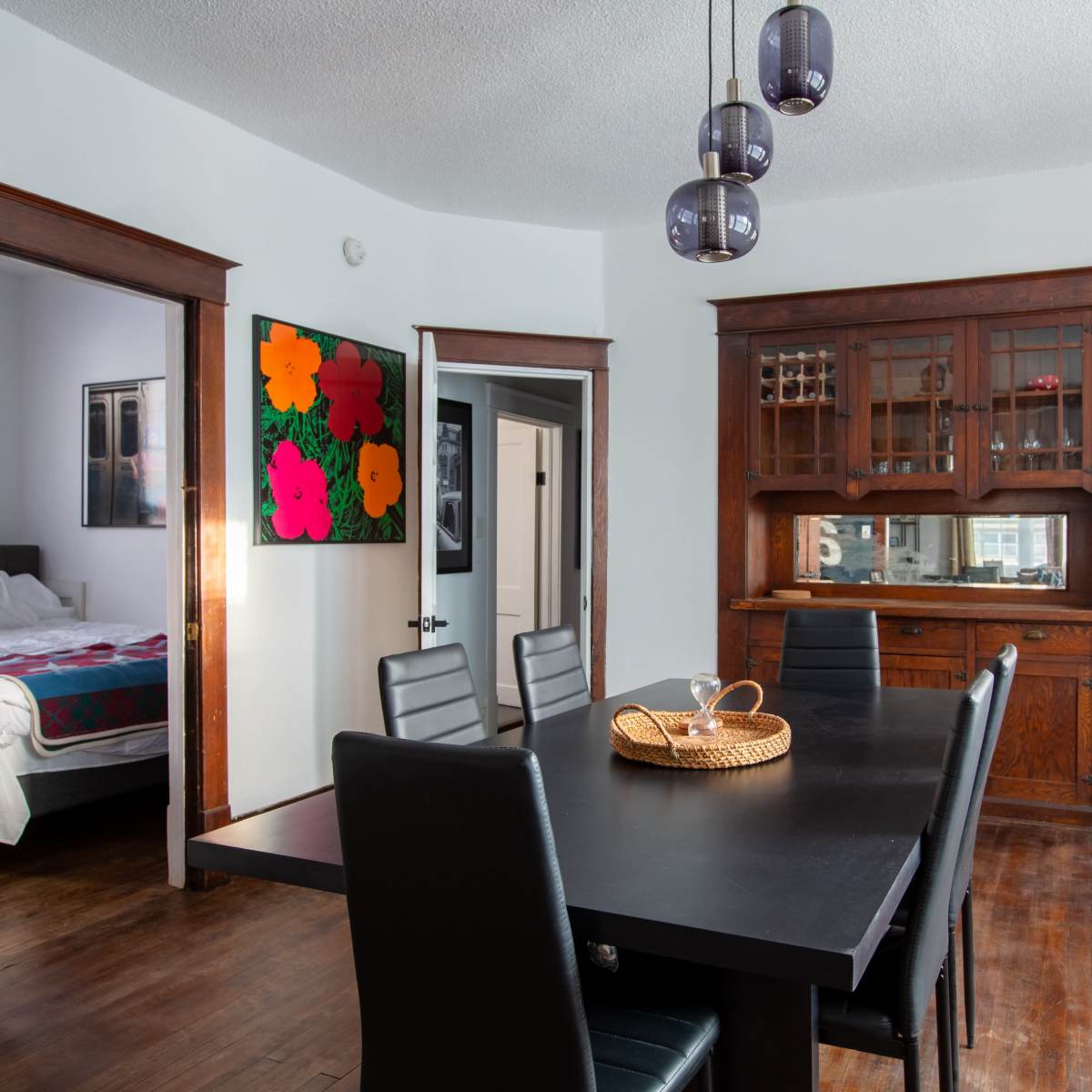 A dining room features a large black table surrounded by chairs, with doors leading to an adjacent room and a sideboard against the wall.