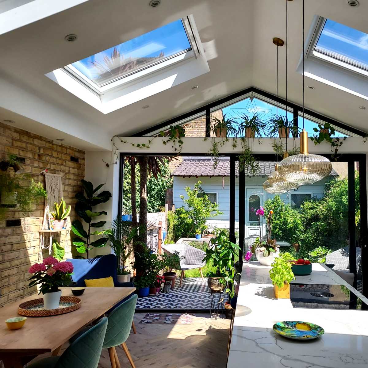 A bright kitchen with skylights, large glass doors opening to a garden, and various indoor plants adorning the space.