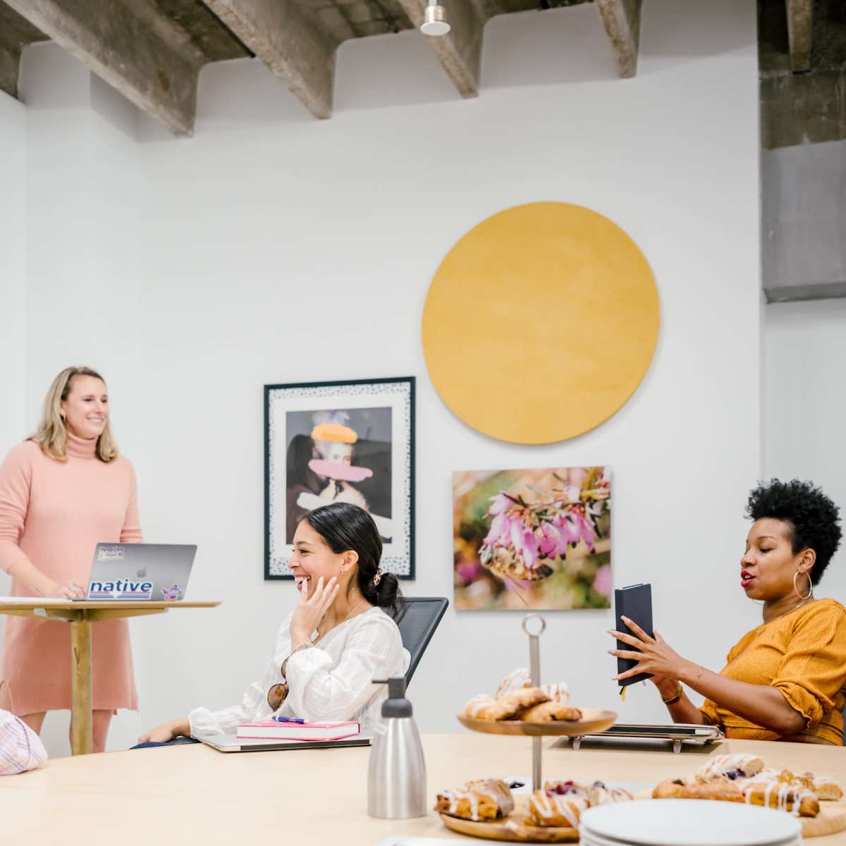A group of people is gathered in a conference room with food on the table while one person presents at the front.