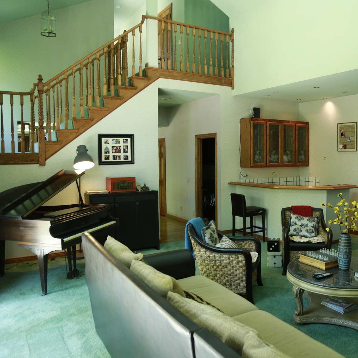 A spacious living room features a grand piano, comfortable seating, and a staircase leading to the upper level.