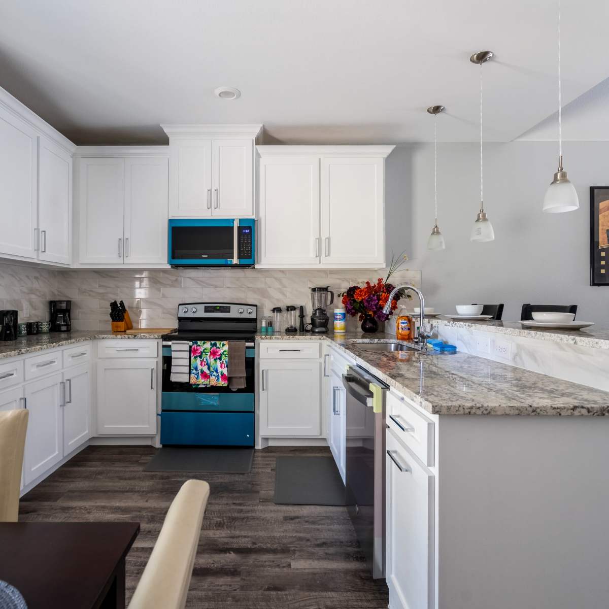 A modern kitchen features white cabinets, granite countertops, and stainless steel appliances with a turquoise oven.