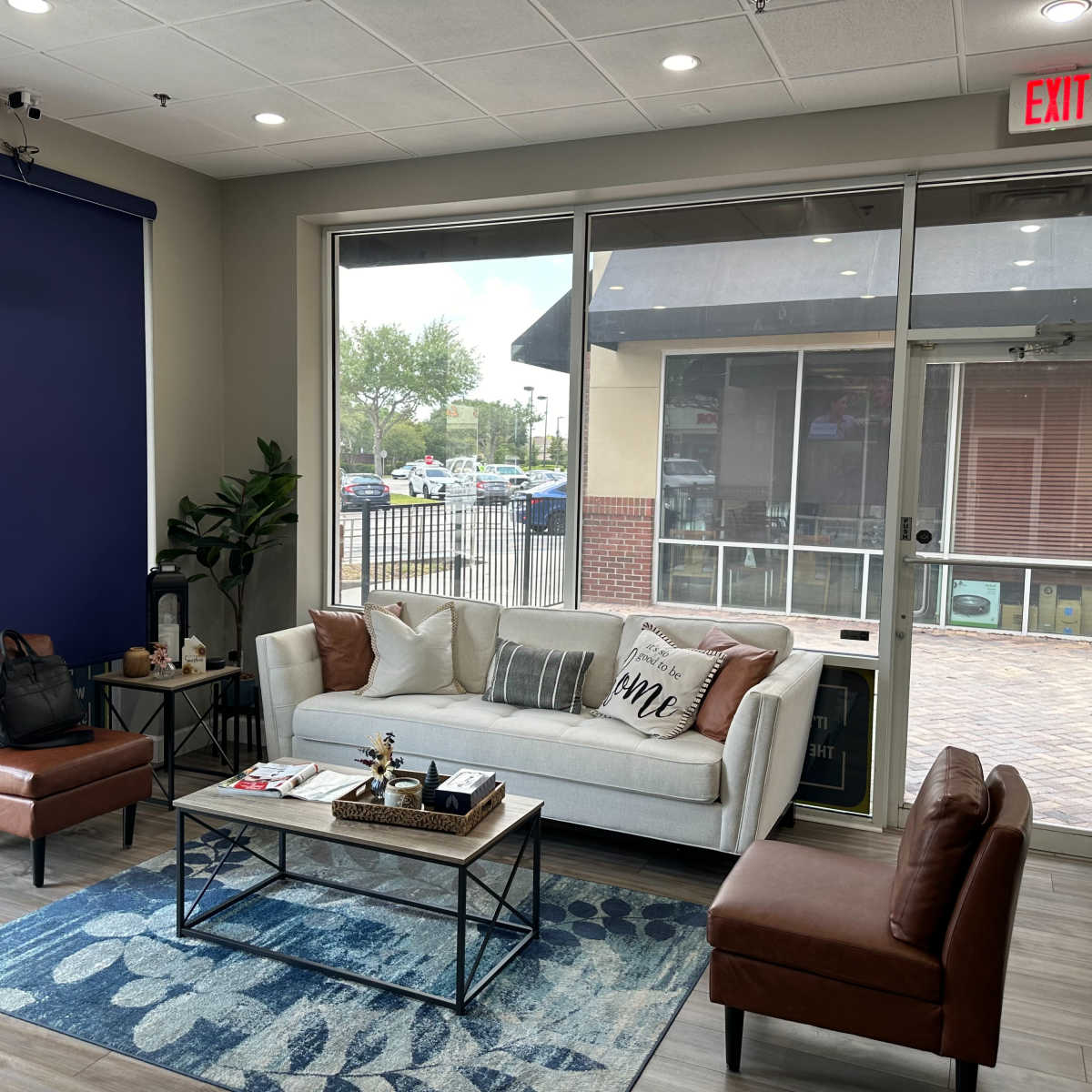 A modern waiting area with a white couch, two brown leather chairs, a coffee table, and large windows overlooking an outdoor space.