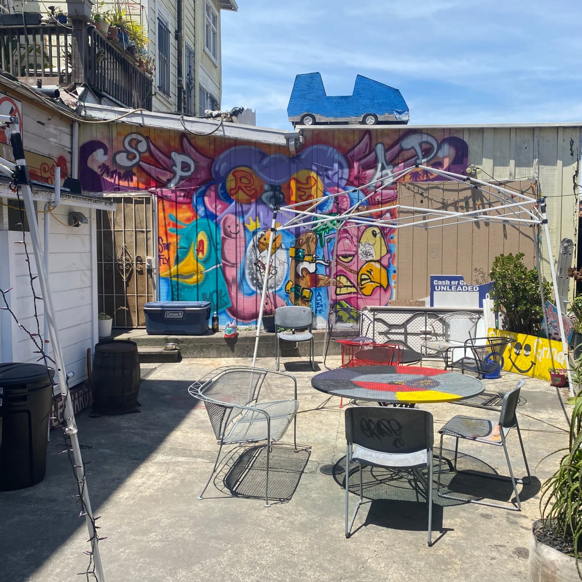 A courtyard with various metal chairs and tables, surrounded by colorful graffiti on the walls.