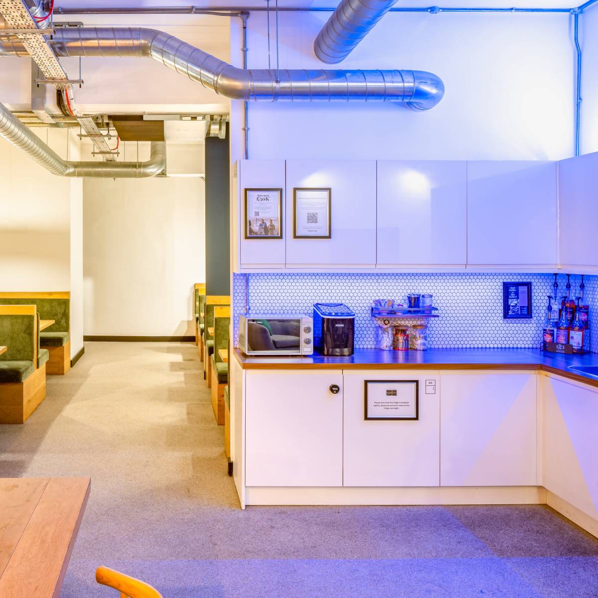 A modern café interior with wooden seating, a kitchenette area, and visible ductwork along the ceiling.