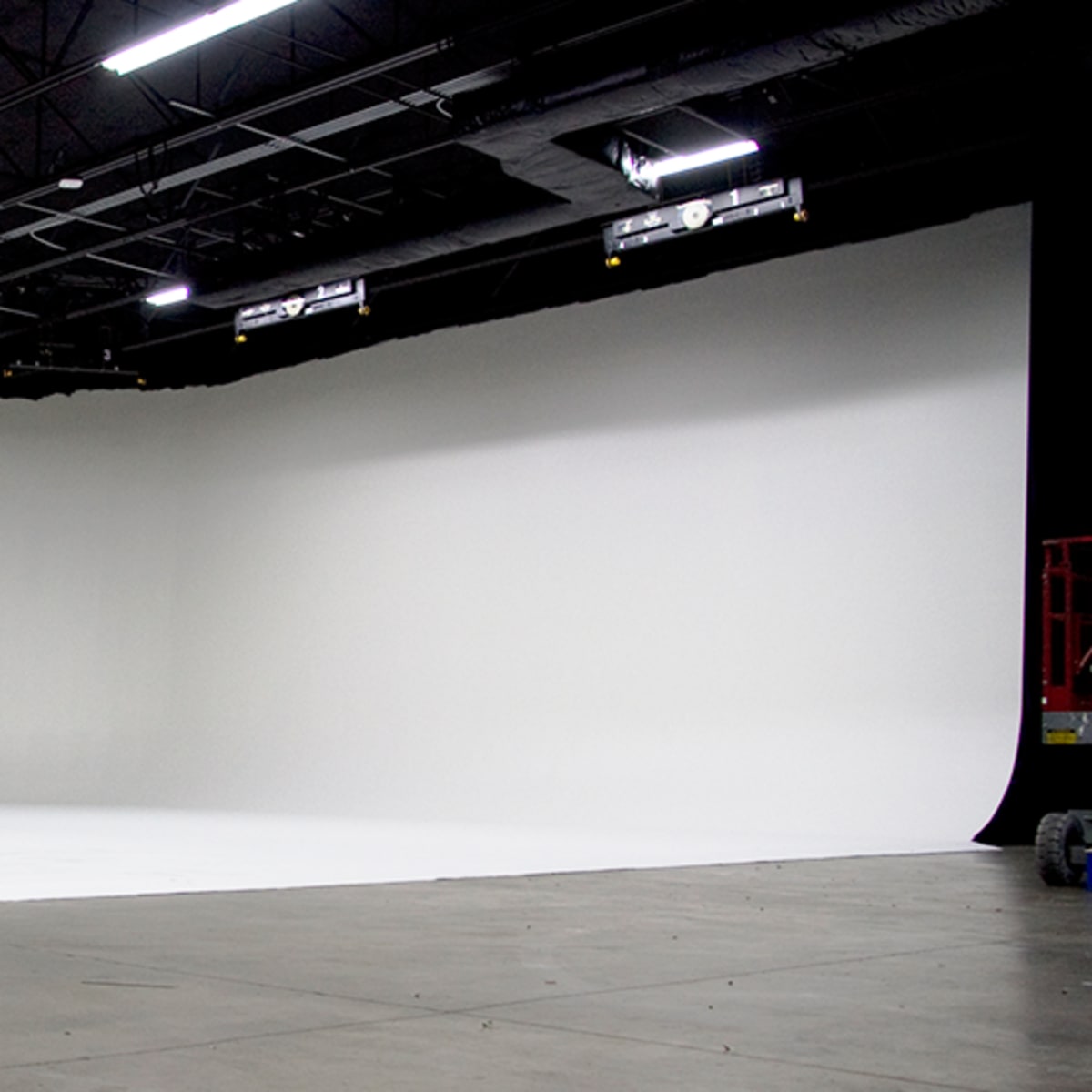 A spacious, empty studio with a seamless white backdrop and overhead lighting.