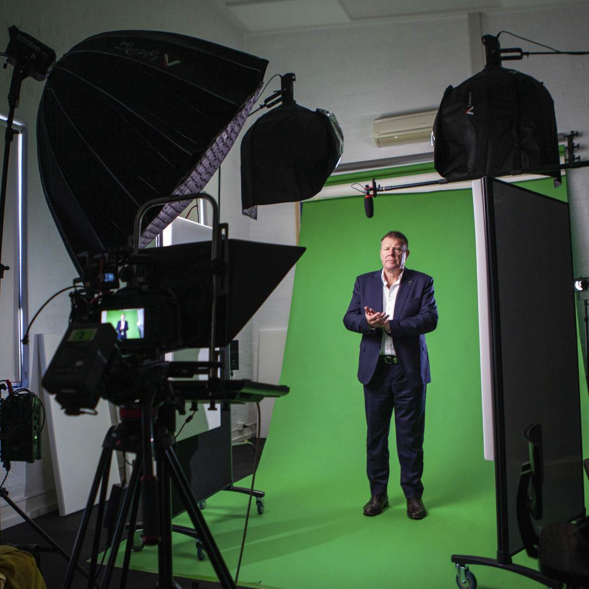 A man stands in front of a green screen inside a studio, surrounded by professional lighting and camera equipment.