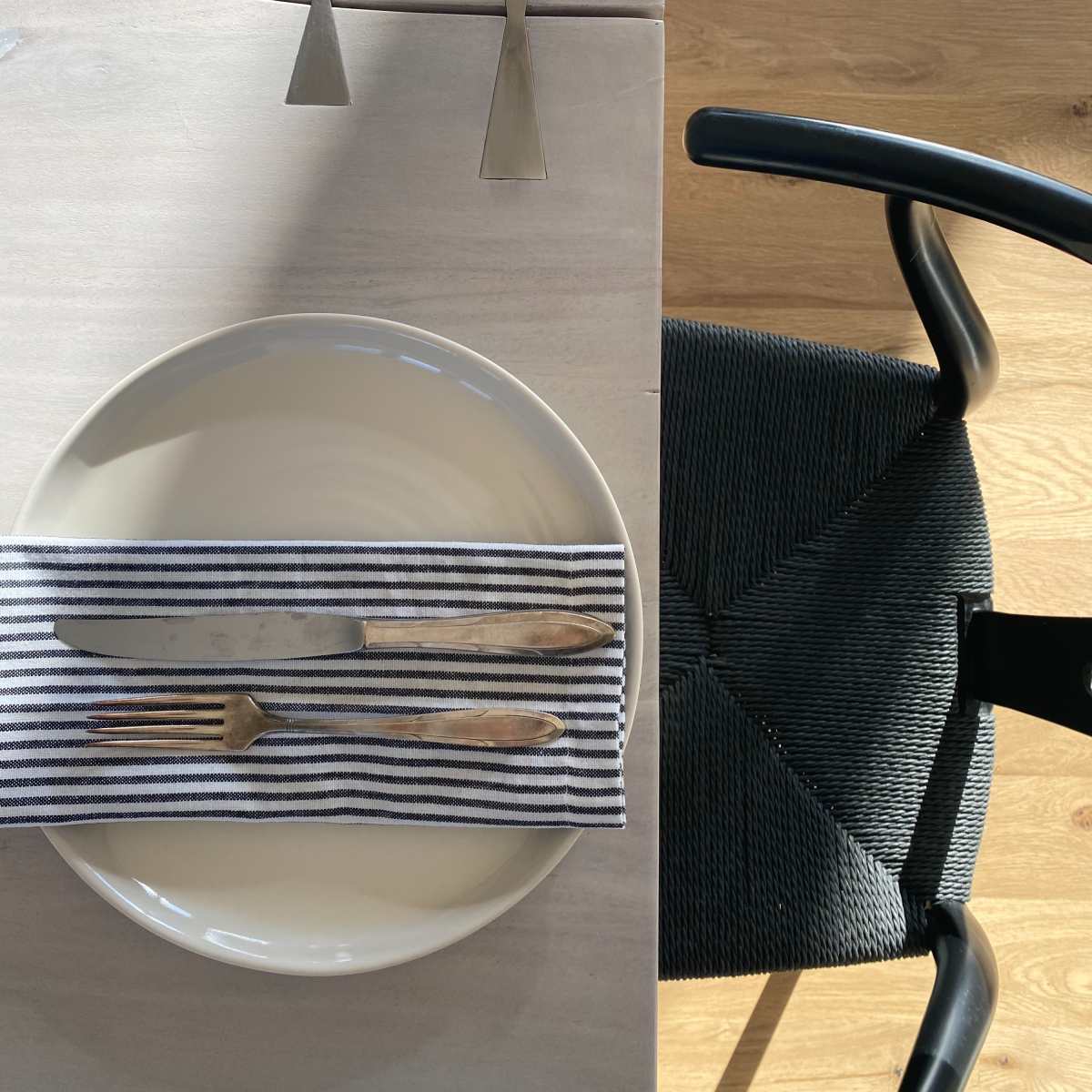 A neatly arranged dining table features a plate on a striped napkin, accompanied by a knife and fork, with modern silverware placed above.