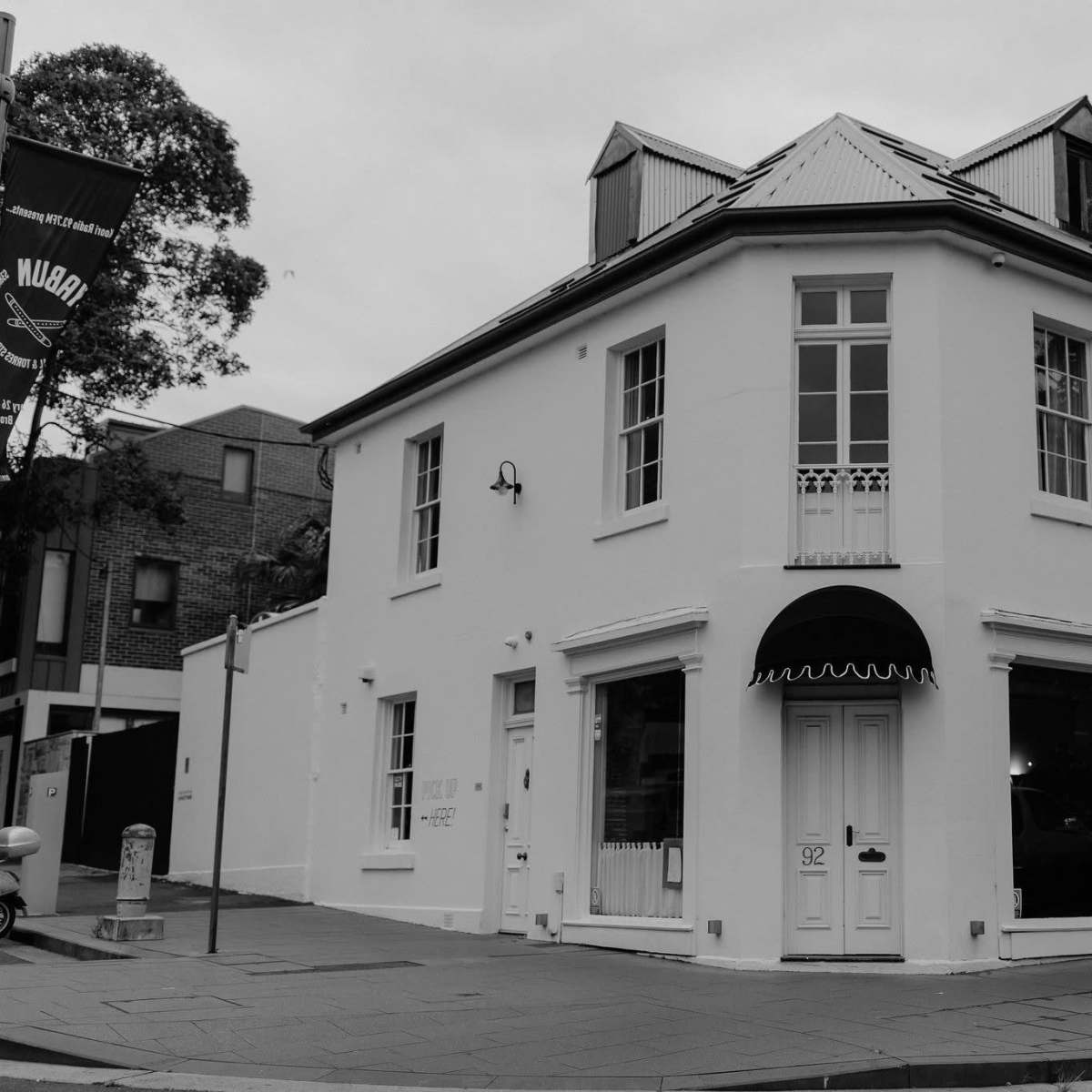 A white, two-story building with large windows, located on a street corner, featuring a black awning above the entrance.