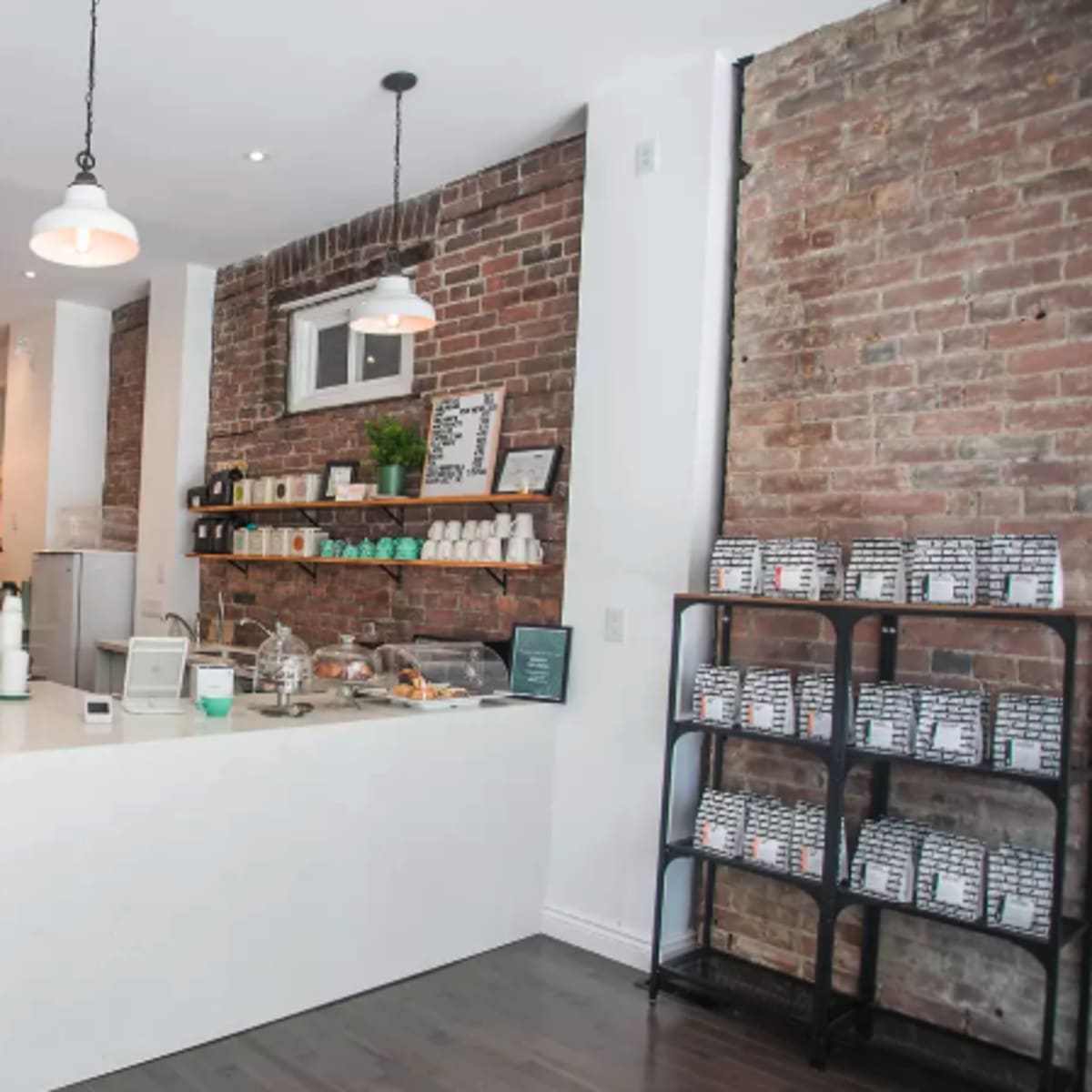 A modern cafe with a sleek white countertop, brick walls, and a display of shelves and seating areas in the background.
