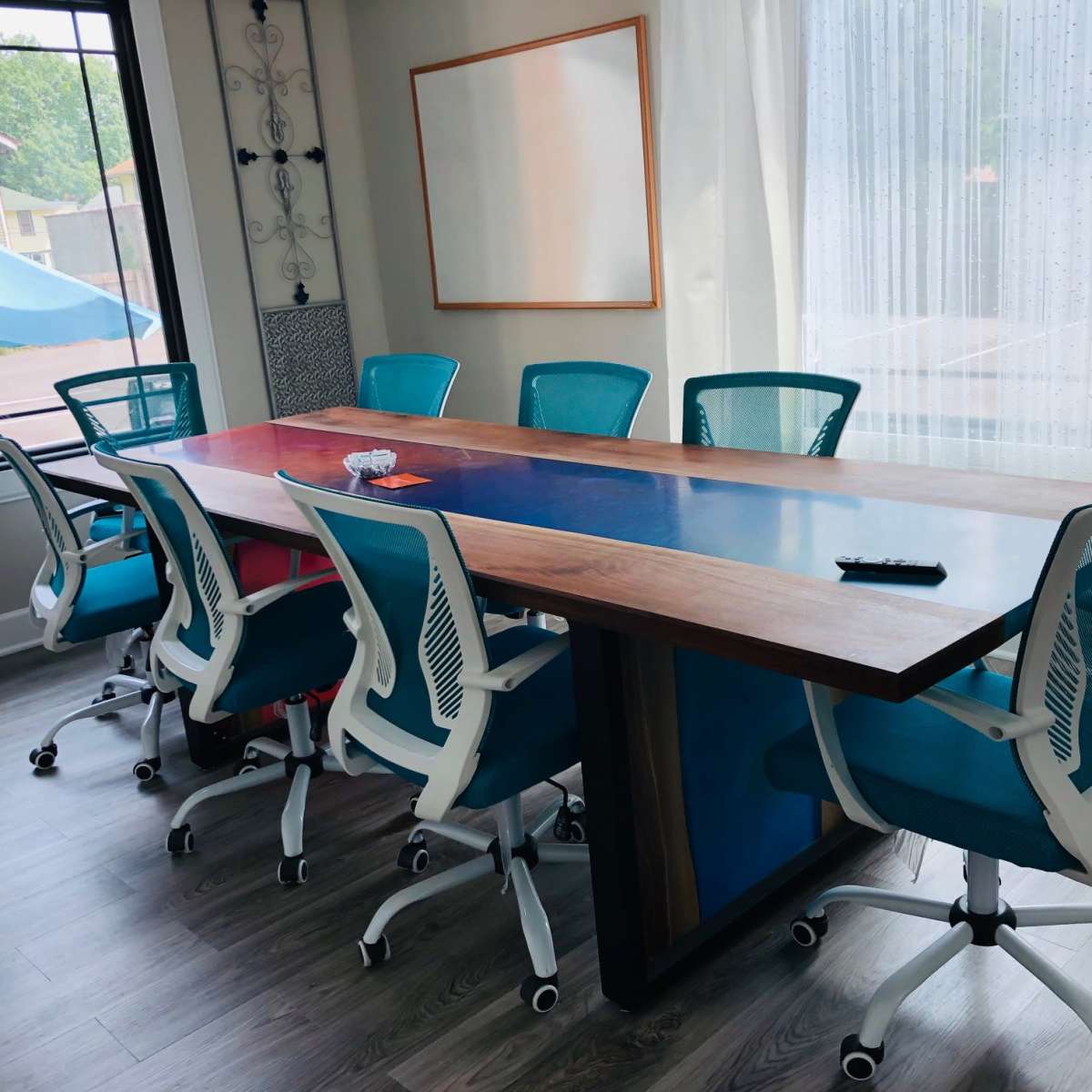 A conference room with a large wooden table and eight blue and white office chairs arranged around it, illuminated by natural light from a window.