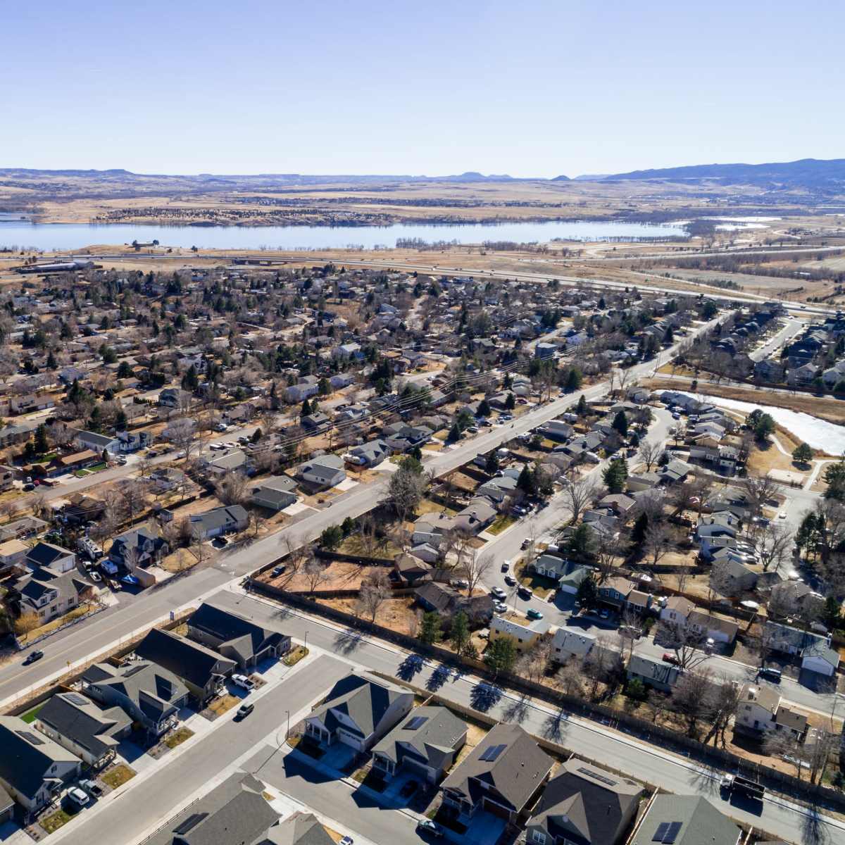 An aerial view of a suburban neighborhood with rows of houses and a nearby body of water under clear skies.