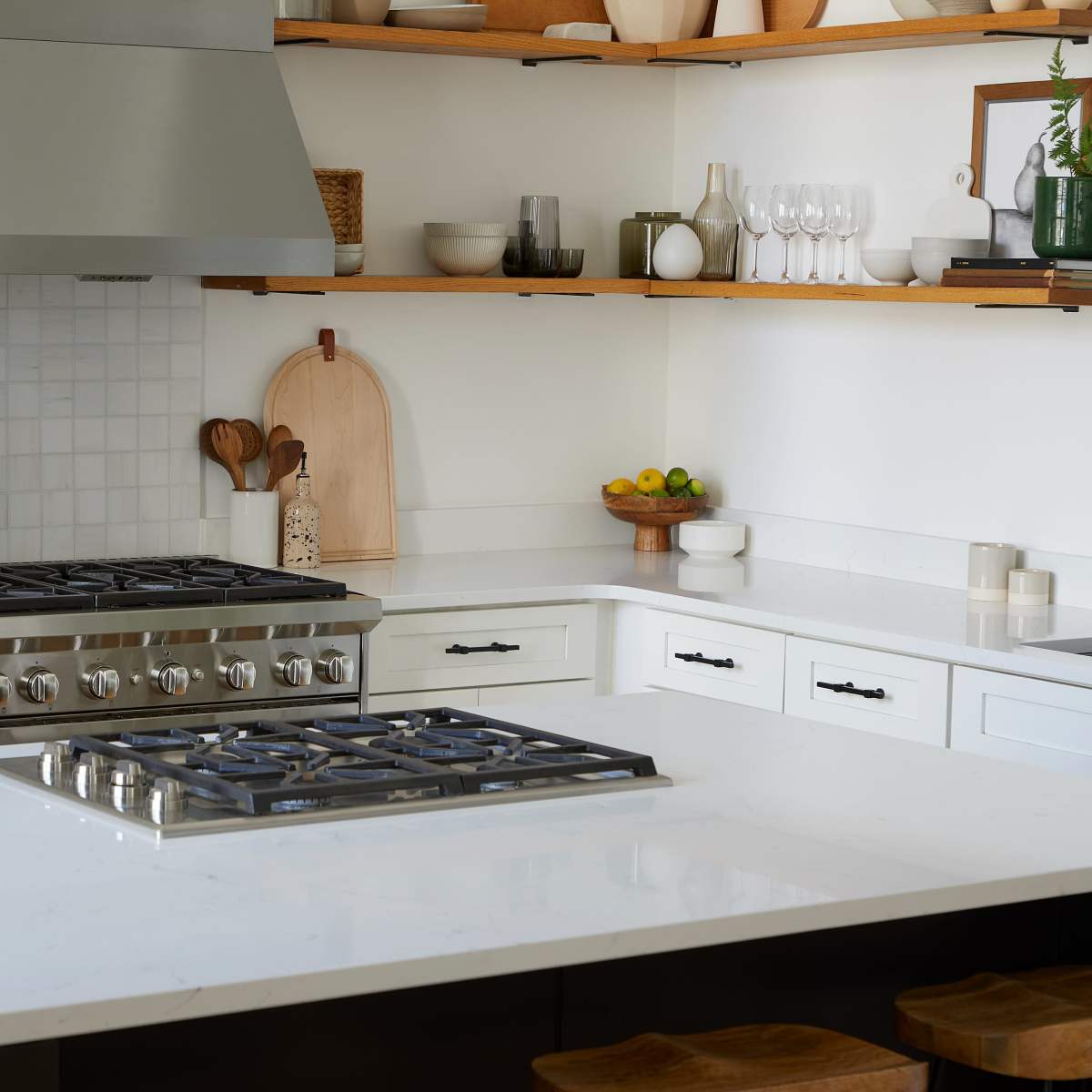 A modern kitchen with a gas stove, white countertops, wooden shelves, and various kitchen items displayed.
