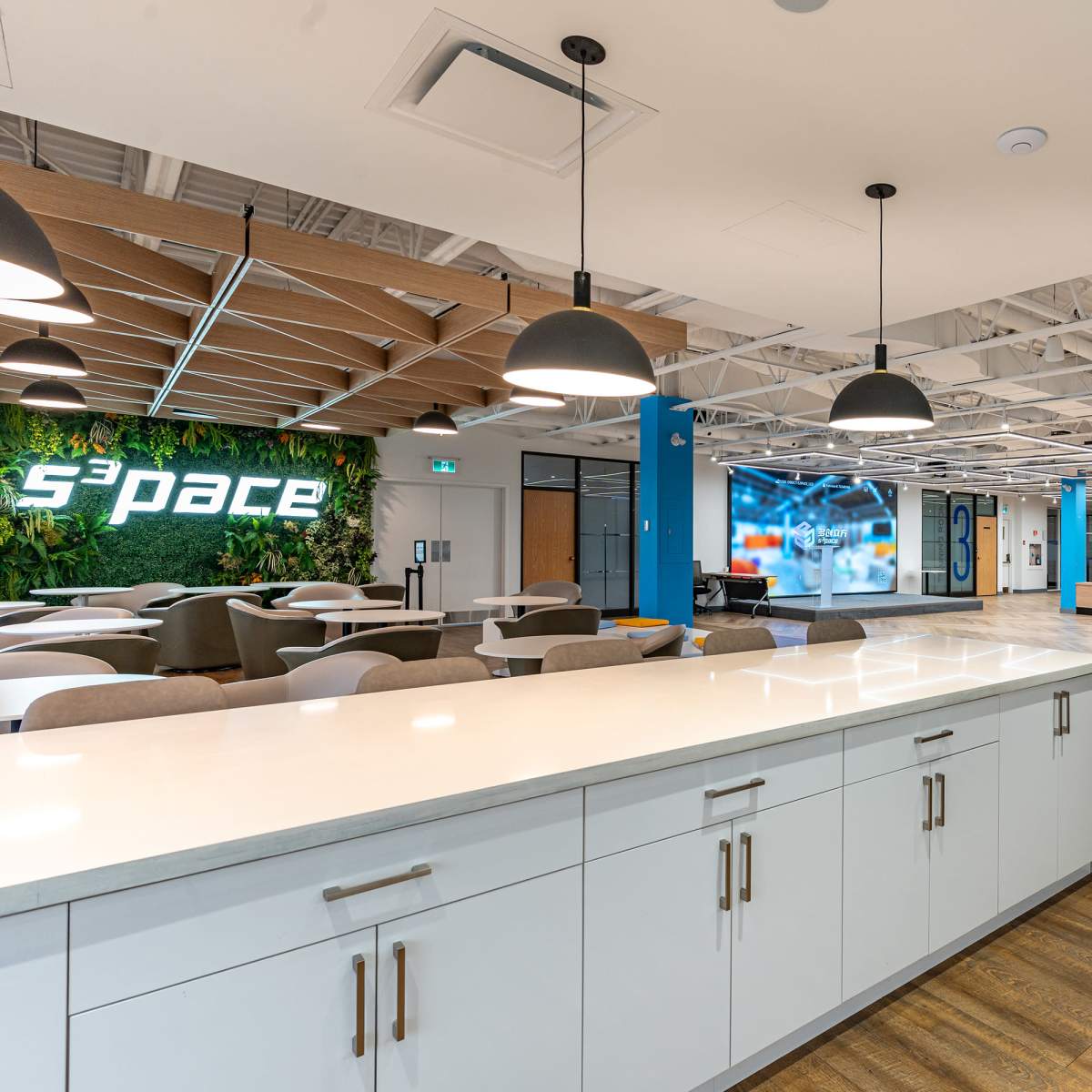 A modern office space featuring a white countertop, seating areas, and vibrant wall decorations, including a logo and digital displays.