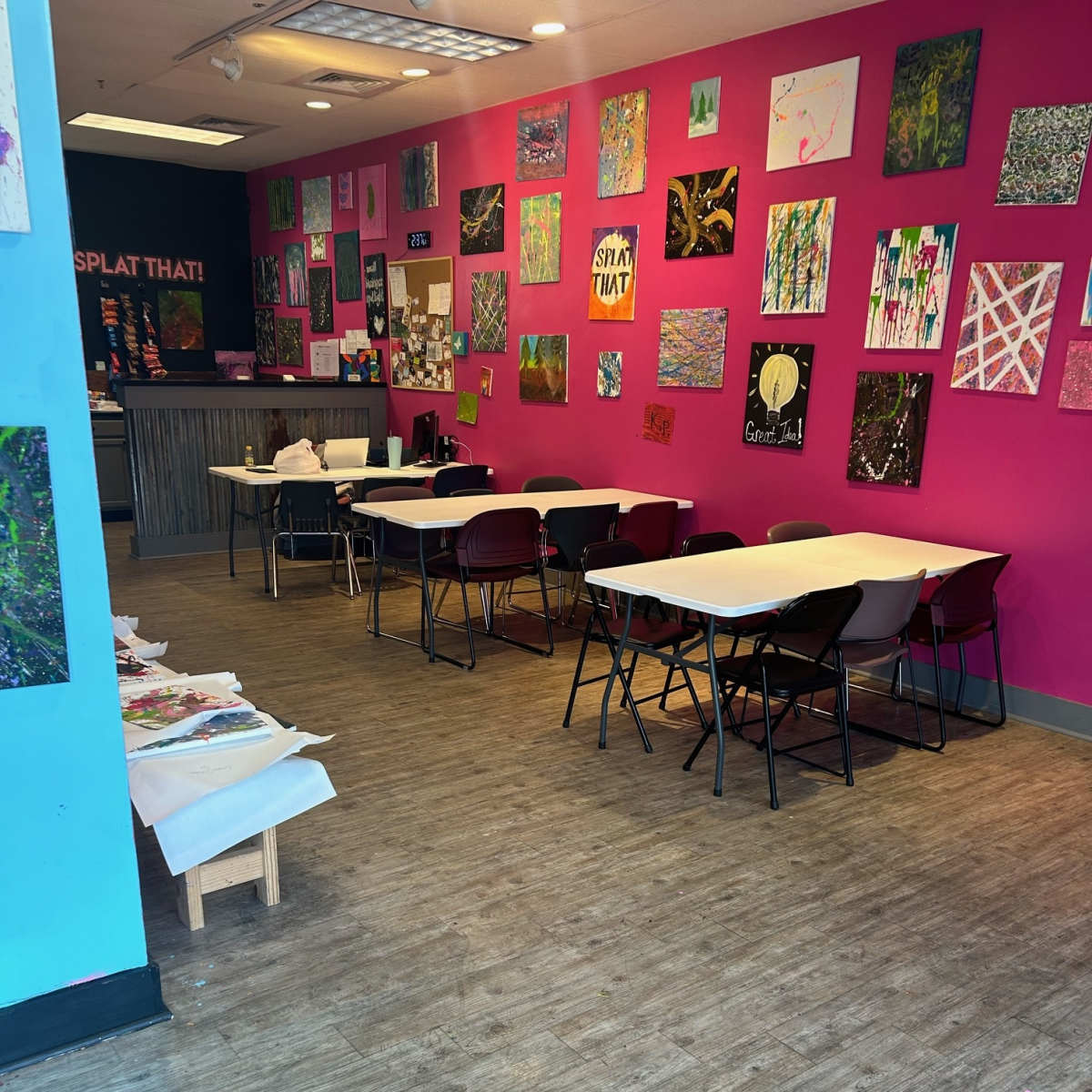 An art studio with pink walls adorned with various artworks and several tables with chairs arranged for activities.
