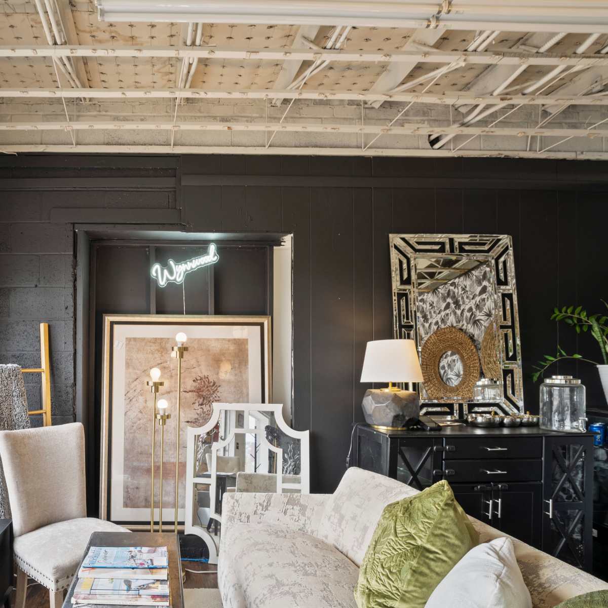 A well-decorated interior space featuring a light-colored sofa, various decorative mirrors, a floor lamp, and a large art piece against a dark wall.