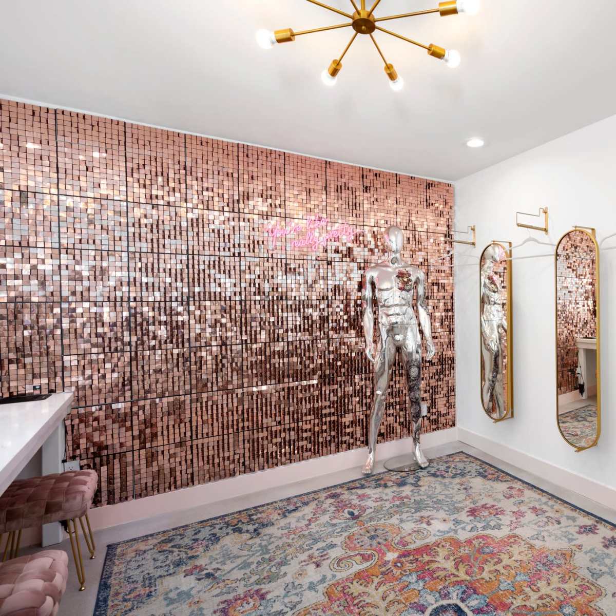 A stylish dressing room featuring a rose gold mirrored wall, sleek mirrors, and a decorative rug.