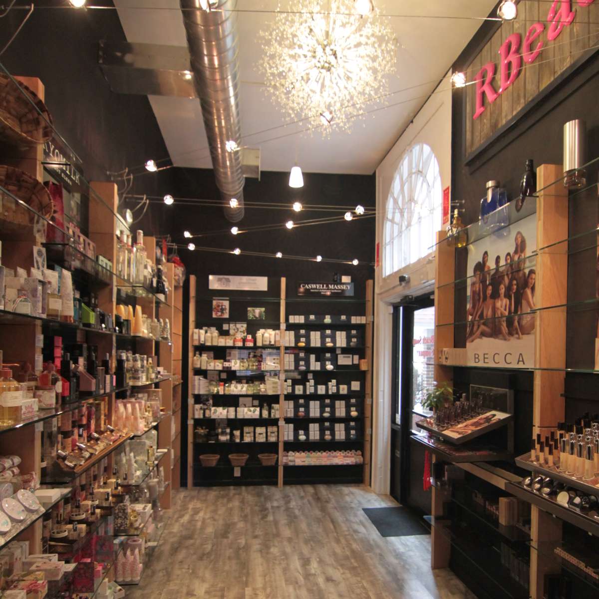 The interior of a retail store features wooden shelves lined with various beauty and personal care products, illuminated by string lights overhead.