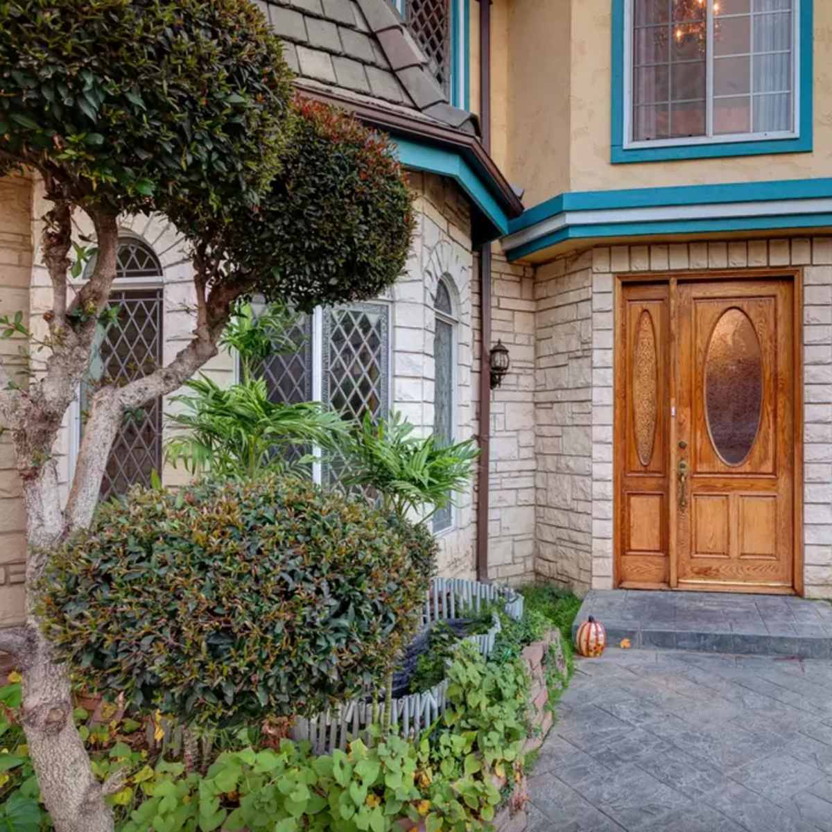 A stone and wood house entrance with double wood doors, surrounded by neatly trimmed shrubs and a landscaped front yard.