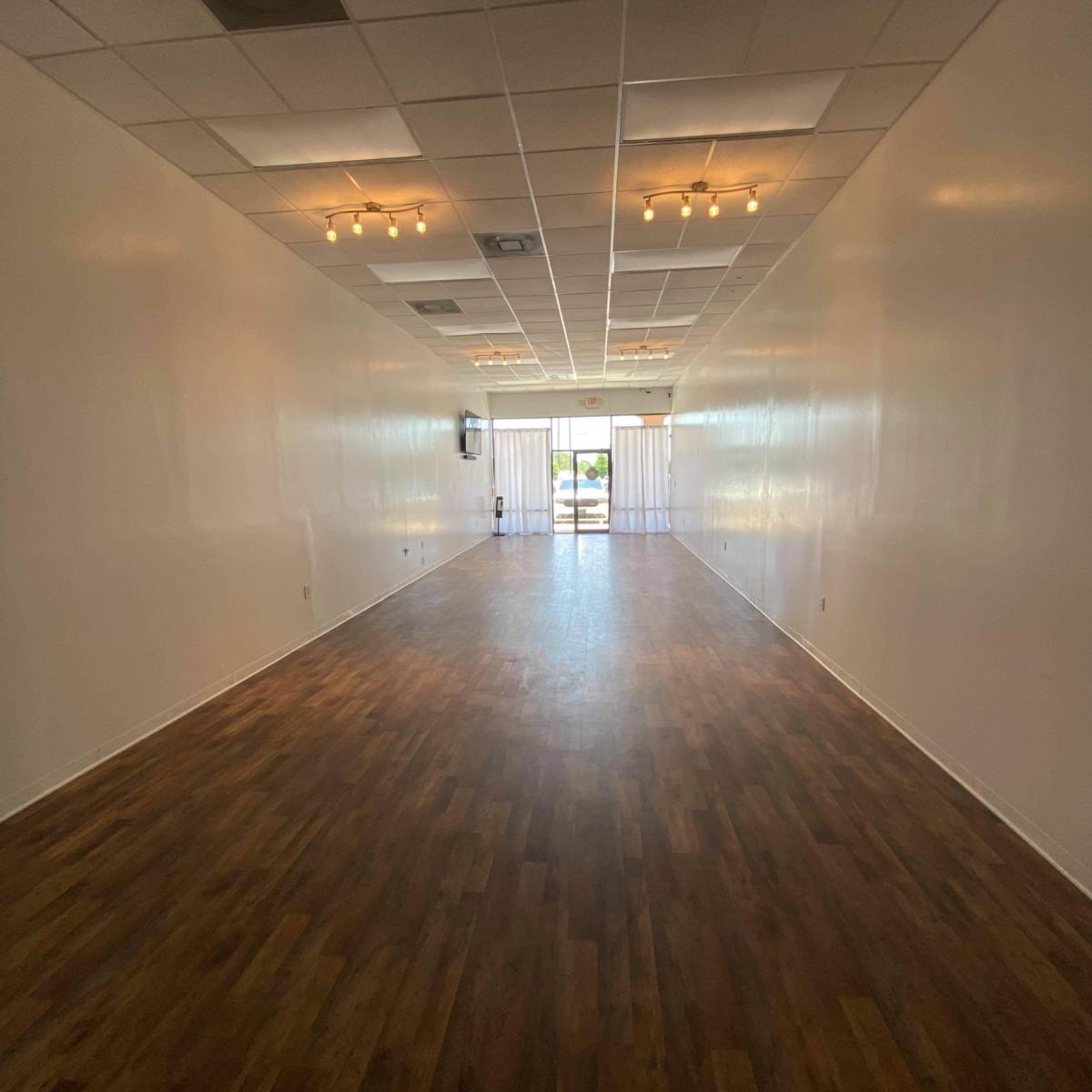 A spacious, empty interior room with wooden flooring and large windows at one end.