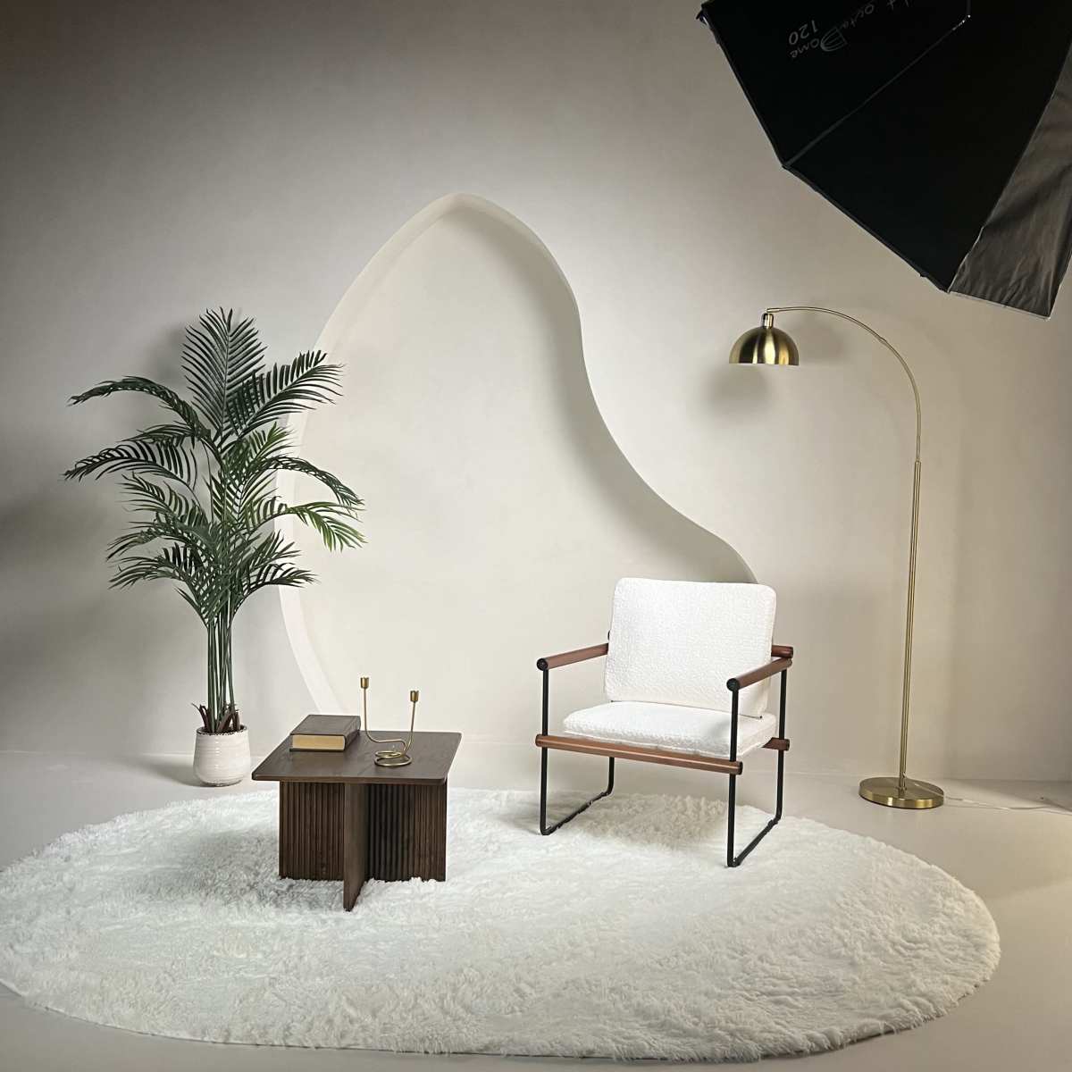 The scene features a minimalist living space with a white rug, a modern armchair, a small wooden table, a floor lamp, and a potted plant, arranged against a textured wall.