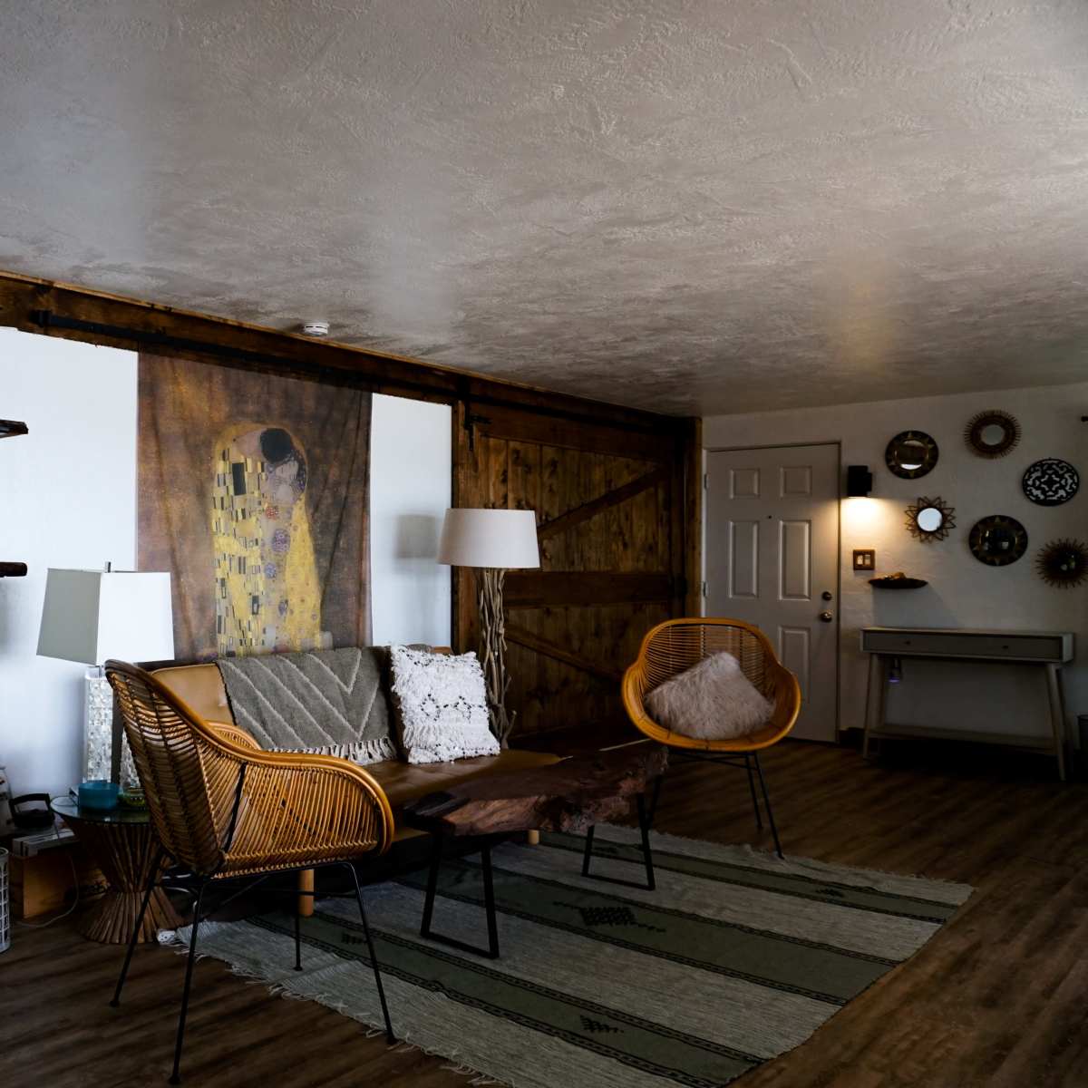 A cozy living room with wooden walls, a coffee table, two rattan chairs, and a decorative wall art piece.