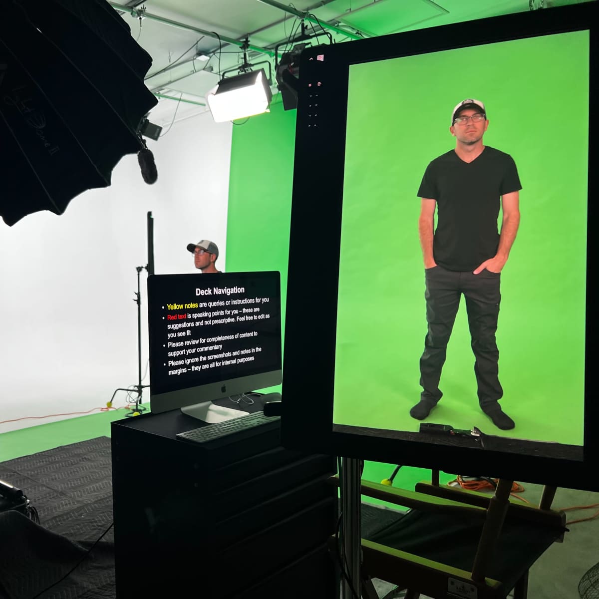 A photoshoot is taking place in a studio with a person standing in front of a green screen while another individual adjusts equipment.